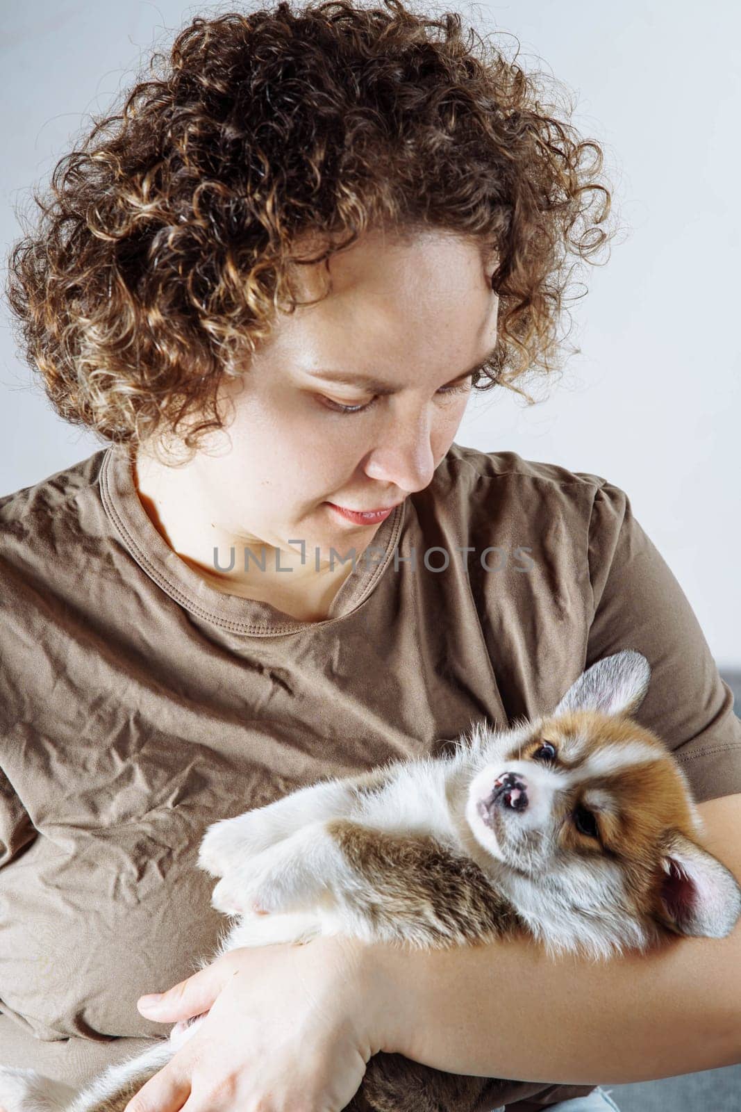 Tenderness and care. Young woman in dark beige cotton T-shirt lovingly hugs cute little Welsh corgi puppy. Dog food. Pets. Dog in family. Features of keeping puppies. Veterinary control.