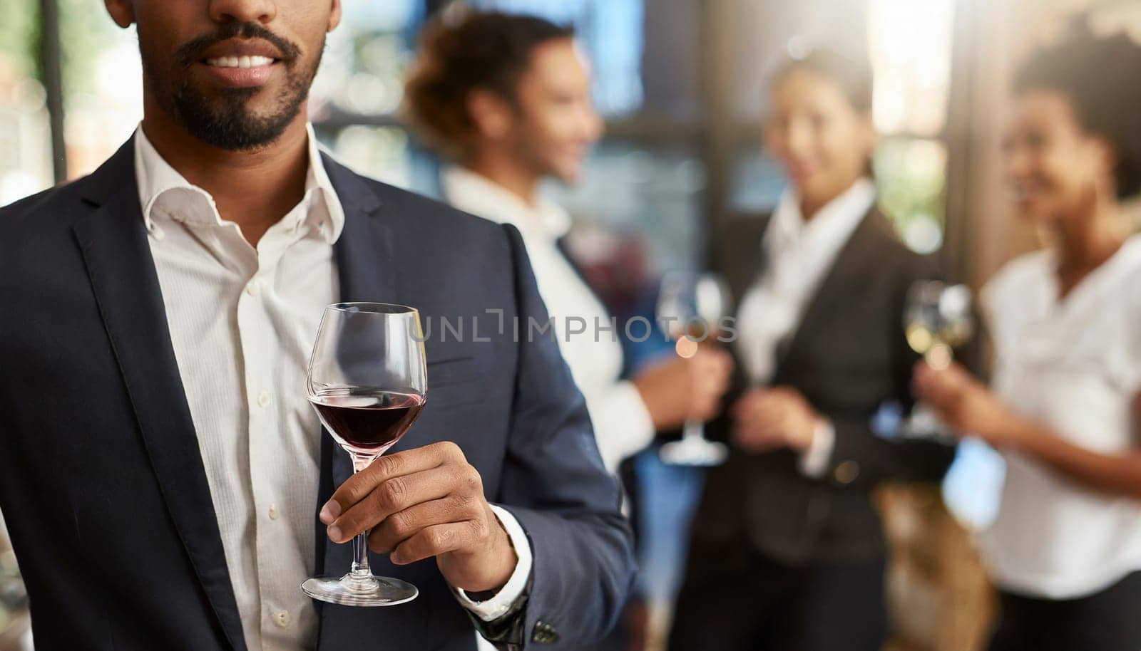 Businessman holding a glass of red wine in the office with colleagues in the background. AI generated