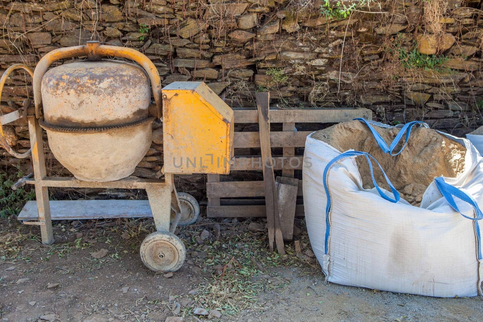 Raffia large sand sack stacked close to cement mixer. Rural residences construction industry concept