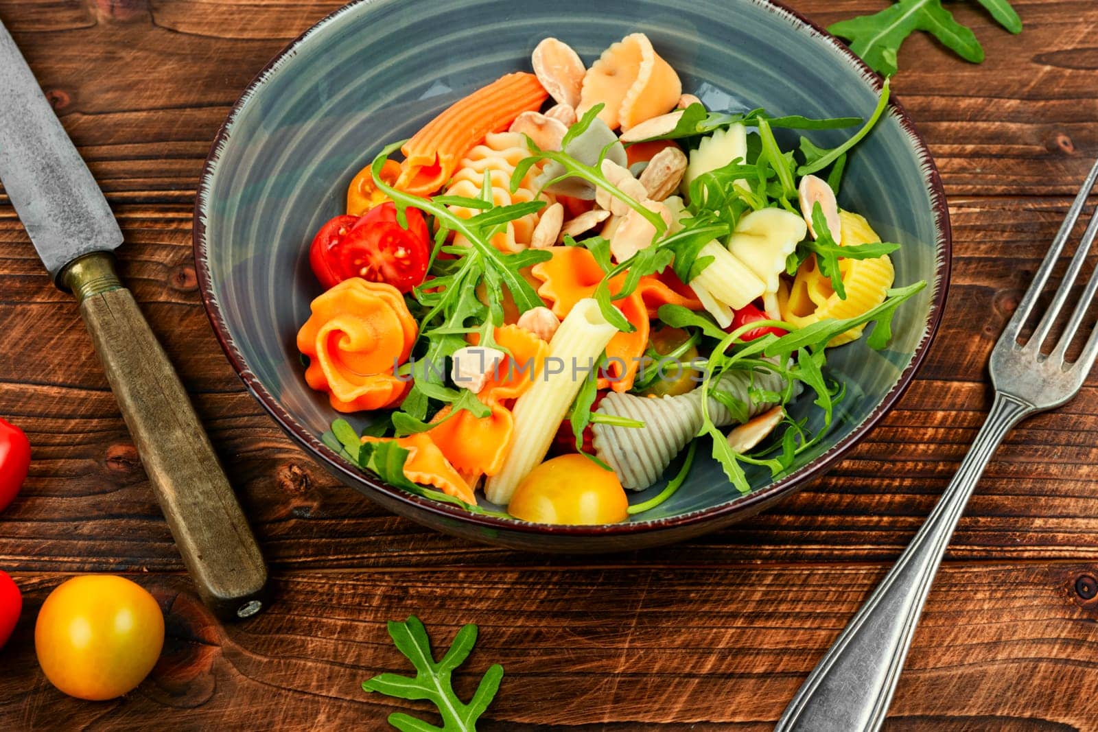 Salad with fresh tomatoes, herbs and pasta in a plate on a dark wooden table .