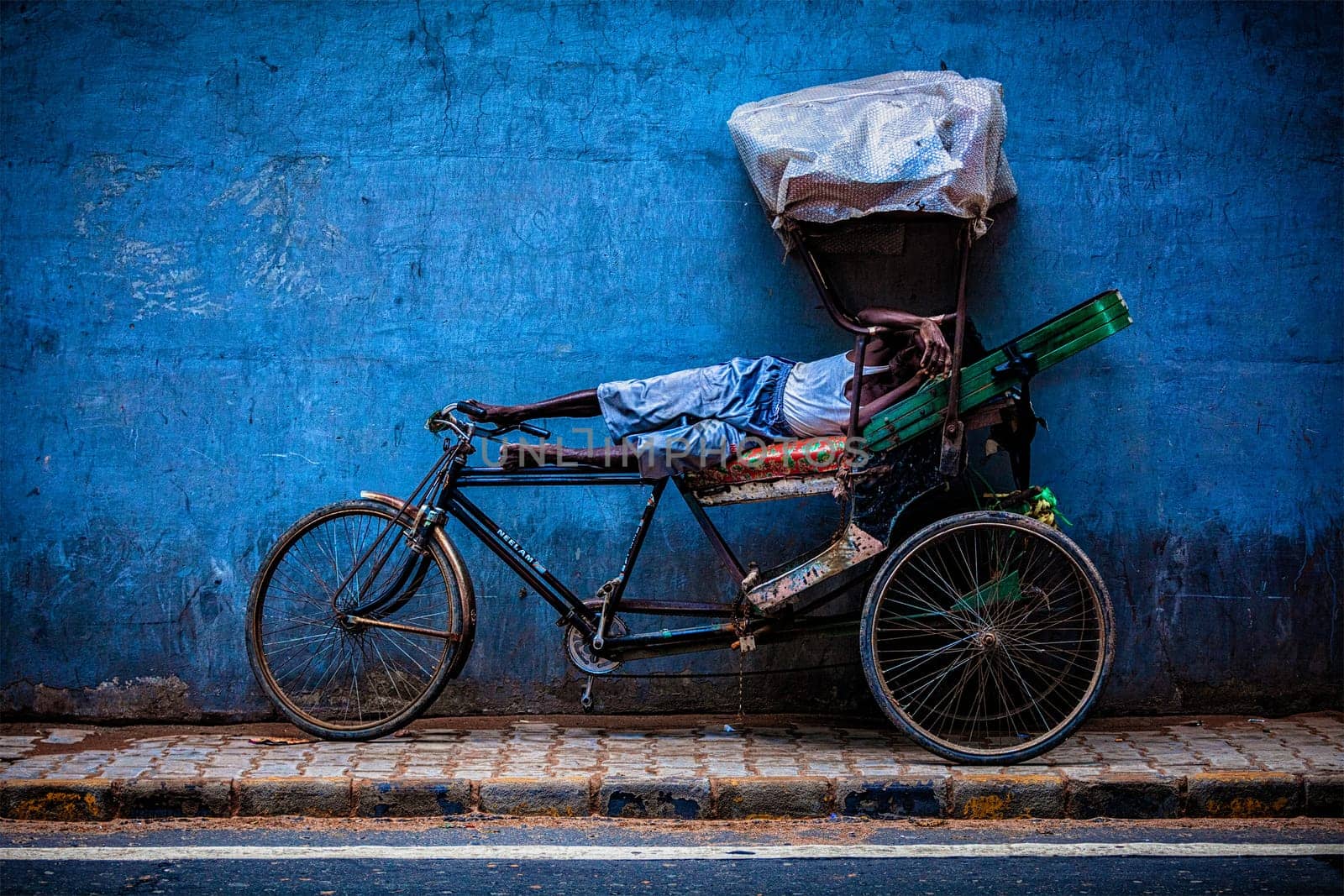 NEW DELHI, INDIA - SEPTEMBER 11, 2011: Indian cycle rickshaw driver sleeping on his bicycle in street. Cycle rickshaws were used in Kolkata since 1930 and are now common in rural and urban areas