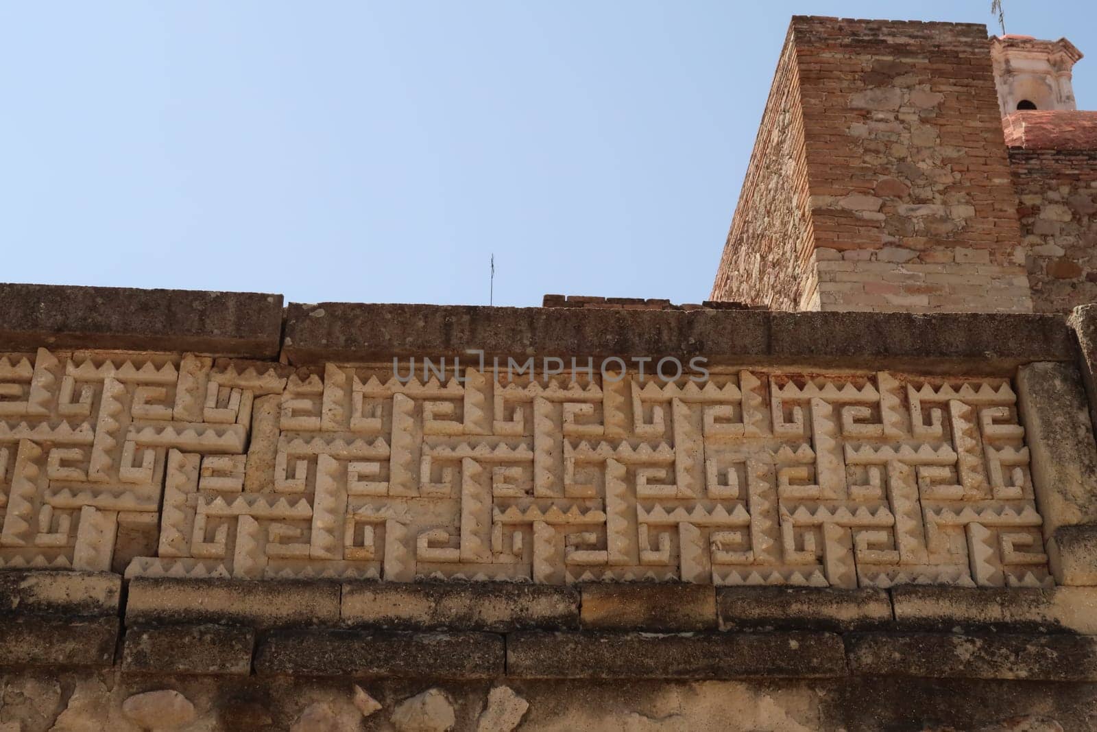 Ornamented ancient Zapotec wall next to the bell tower of the church of San Pablo Villa de Mitla at the archeological site of Mitla, Oaxaca, Mexico 2022