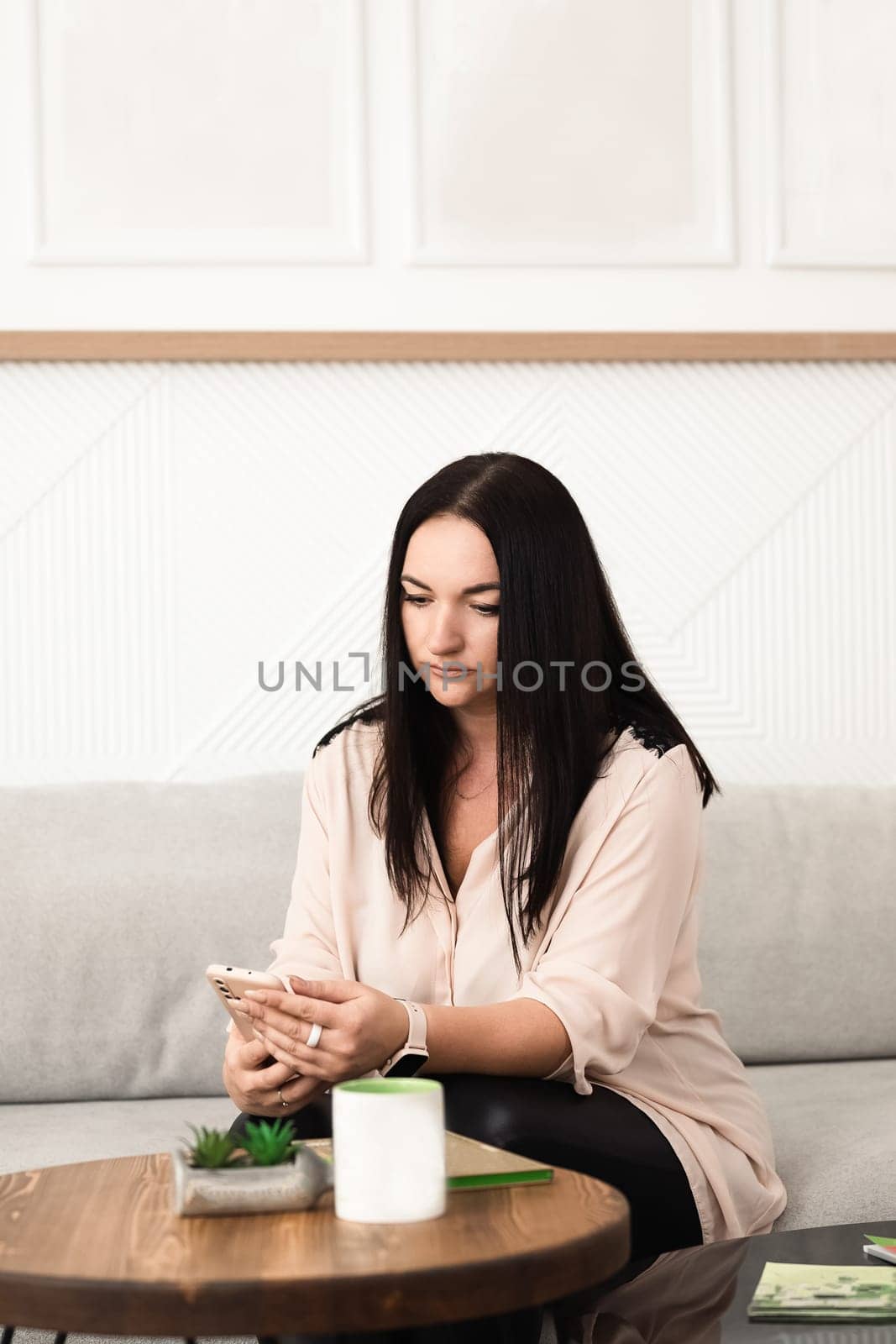 A brunette girl uses a mobile phone app, plays games, makes purchases online, orders delivery, relaxes on the couch.