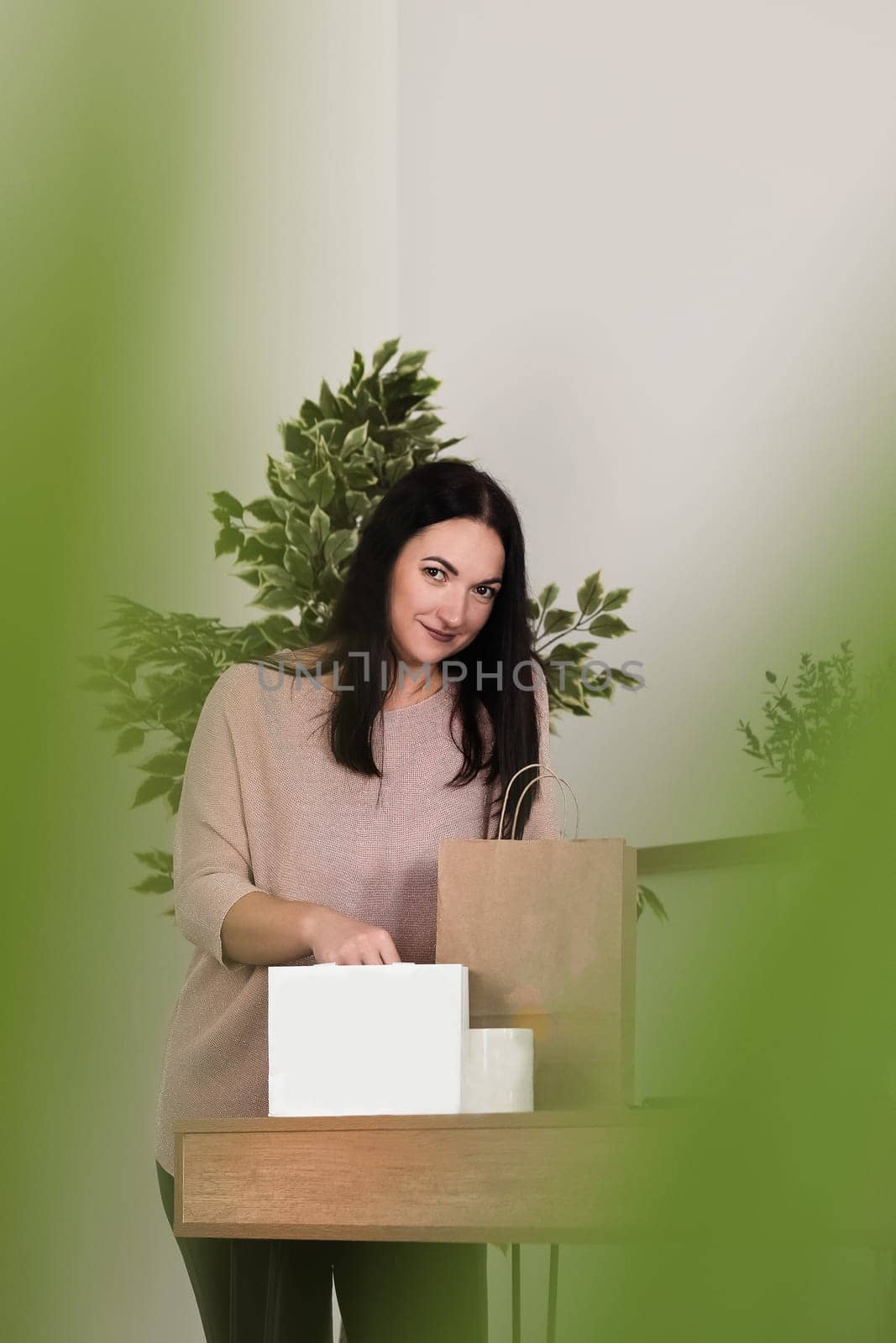 A brunette girl stands at a desk in the office with paper bags and a ceramic mug