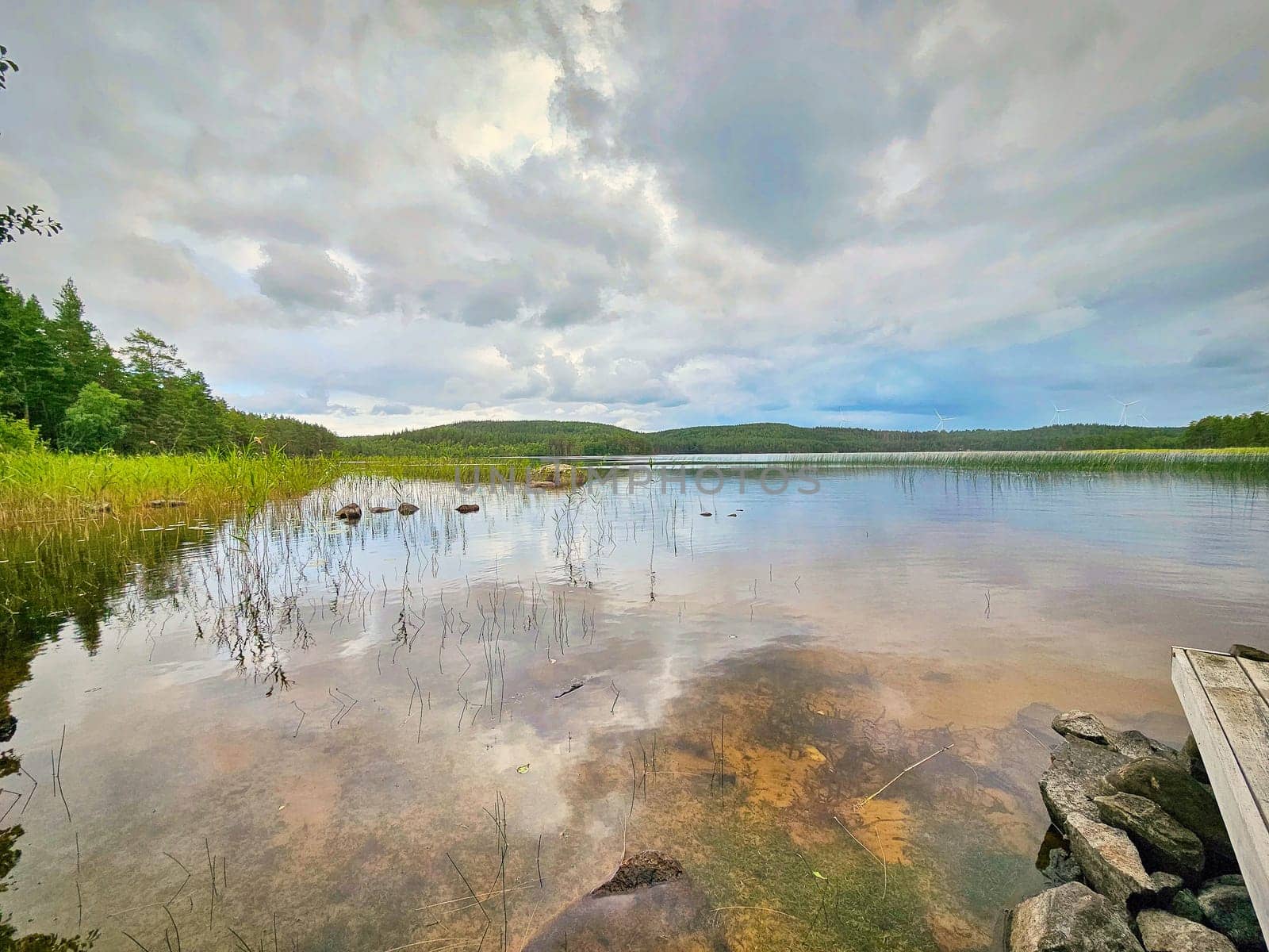 View of a lake in Smaland in Sweden. Blue water with light waves and reeds. Blue sky with veil clouds. Summer in nature in Scandinavia. Landscape photo