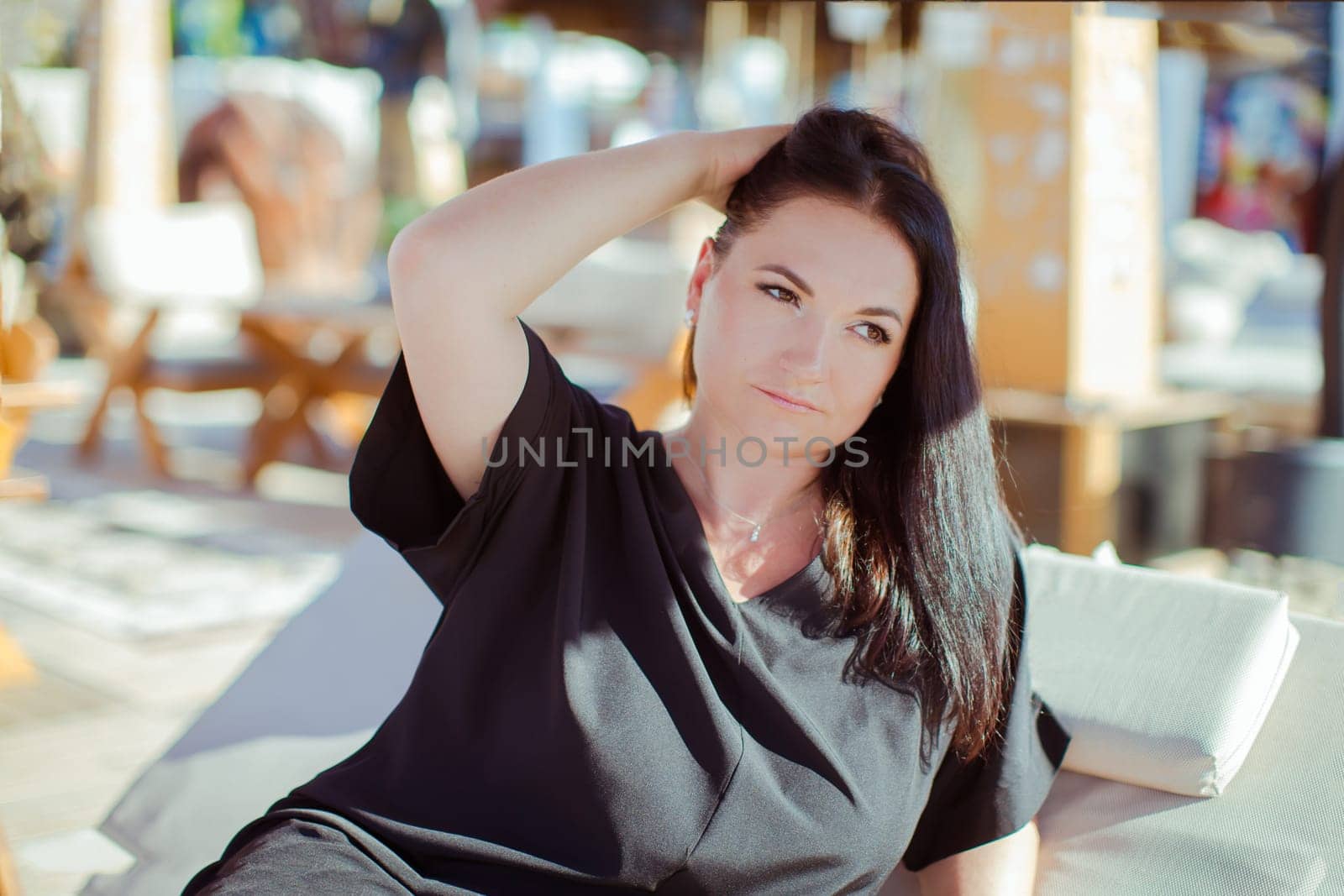 A brunette woman in a black dress is relaxing in a tent on the beach
