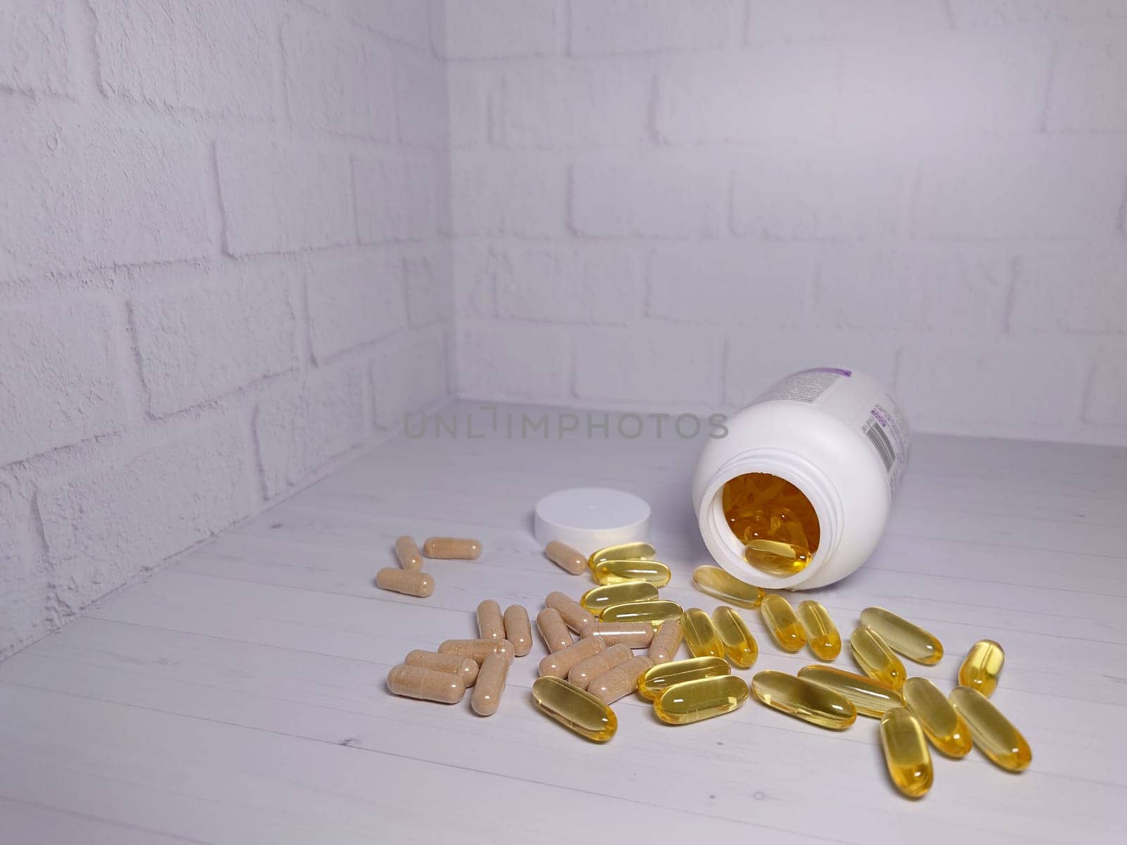 A bottle with pills in capsules of golden and brown color scattered on a light background close-up