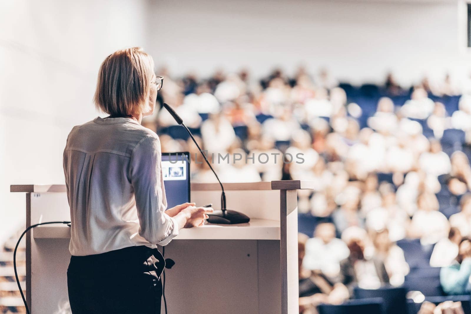 Female speaker giving a talk on corporate business conference. Unrecognizable people in audience at conference hall. Business and Entrepreneurship event