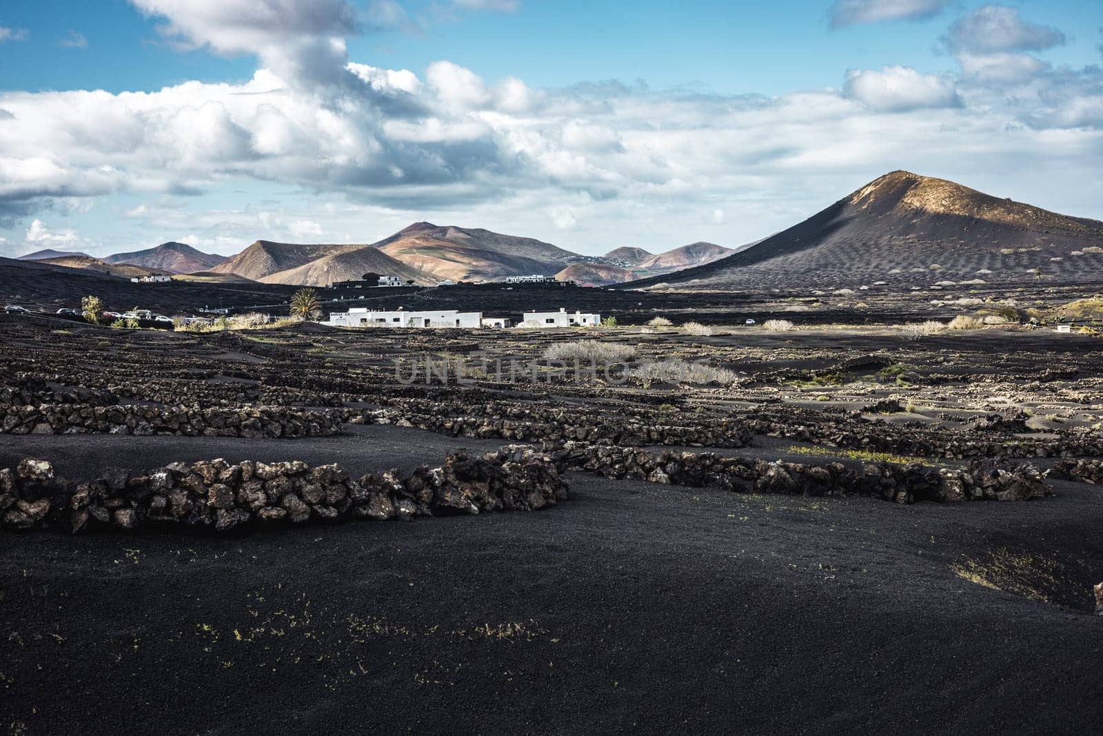 Traditional white houses in black volcanic landscape of La Geria wine growing region with view of Timanfaya National Park in Lanzarote. Touristic attraction in Lanzarote island, Canary Islands, Spain
