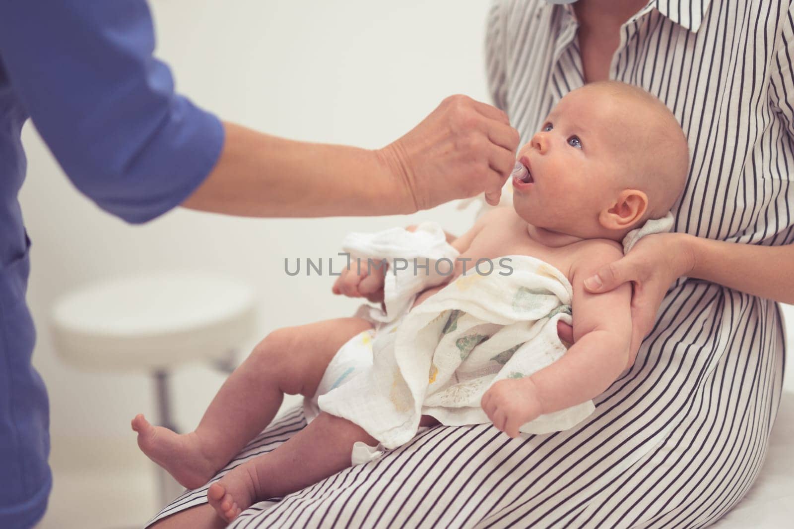 Pediatrician administring oral vaccination against rotavirus infection to little baby in presence of his mother. Children health care and disease prevention.