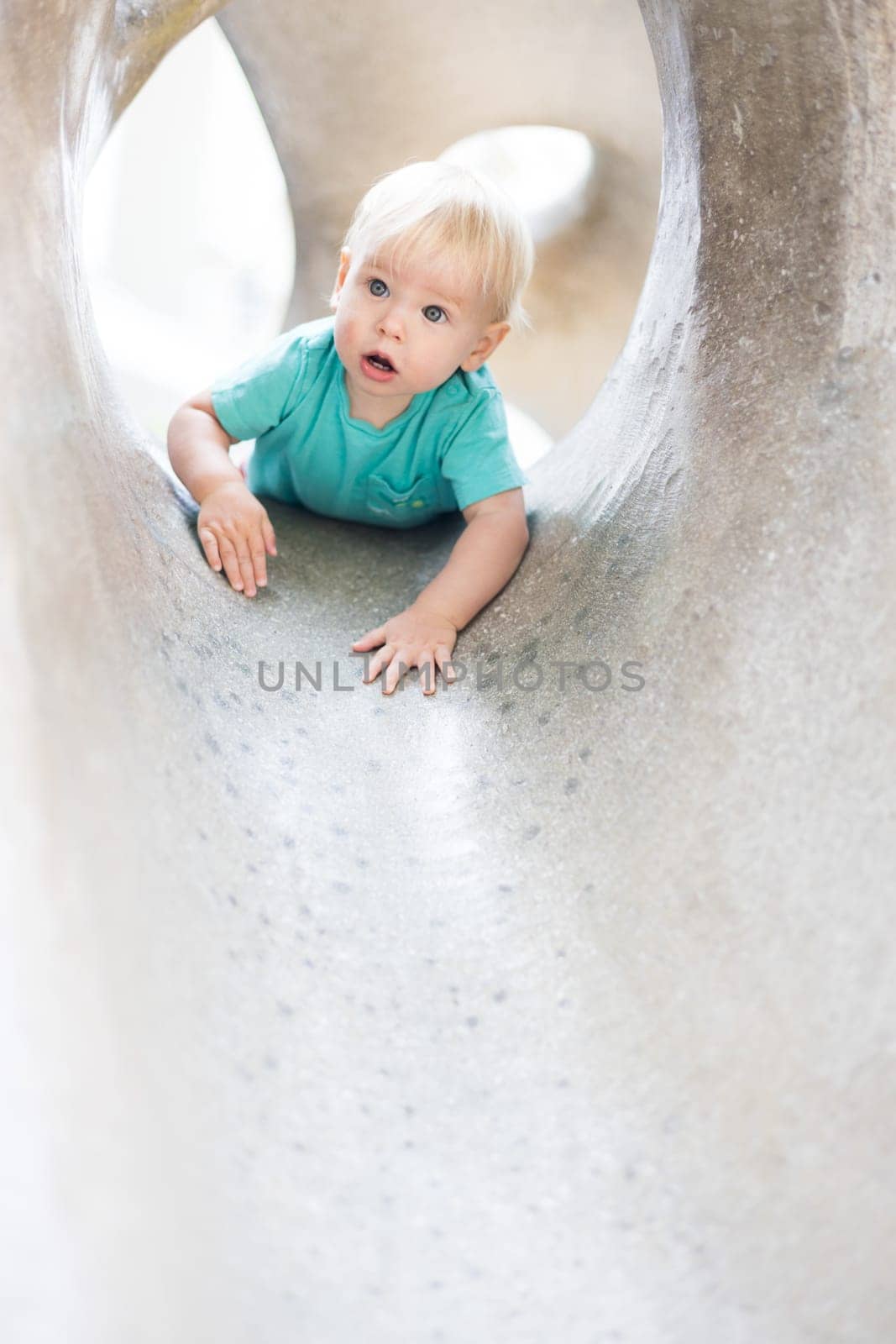 Child playing on outdoor playground. Toddler plays on school or kindergarten yard. Active kid on stone sculpured slide. Healthy summer activity for children. Little boy climbing outdoors