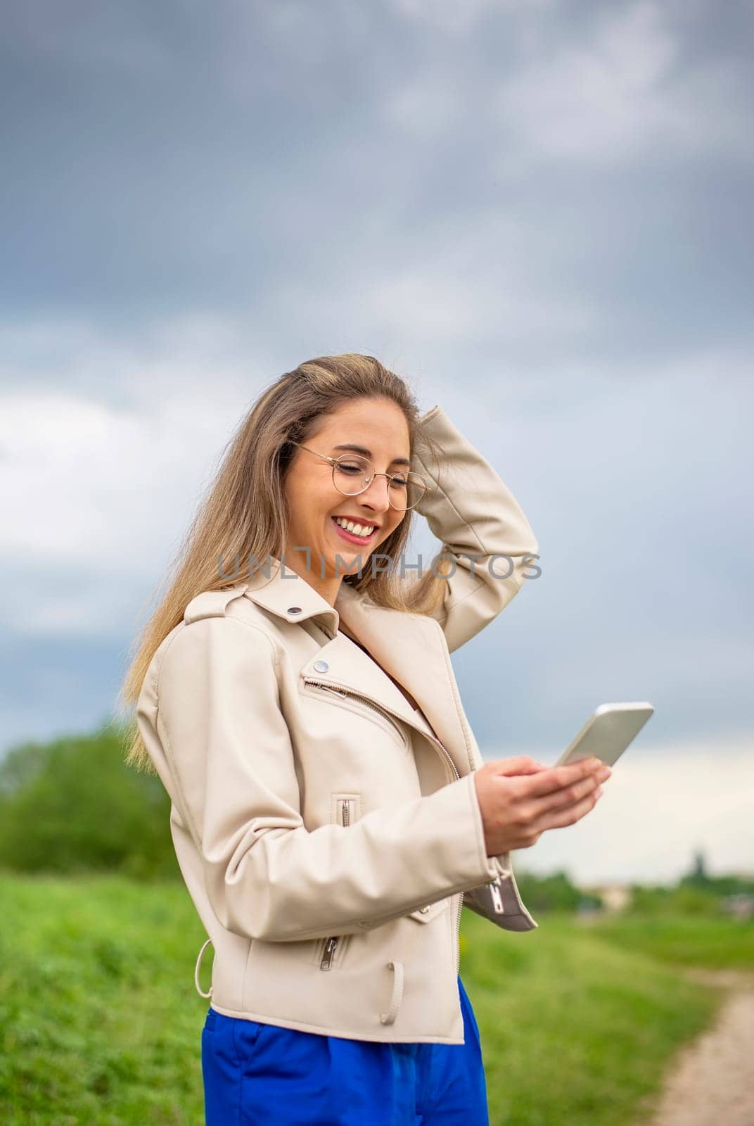 laughing young woman with smartphone standing on a meadow