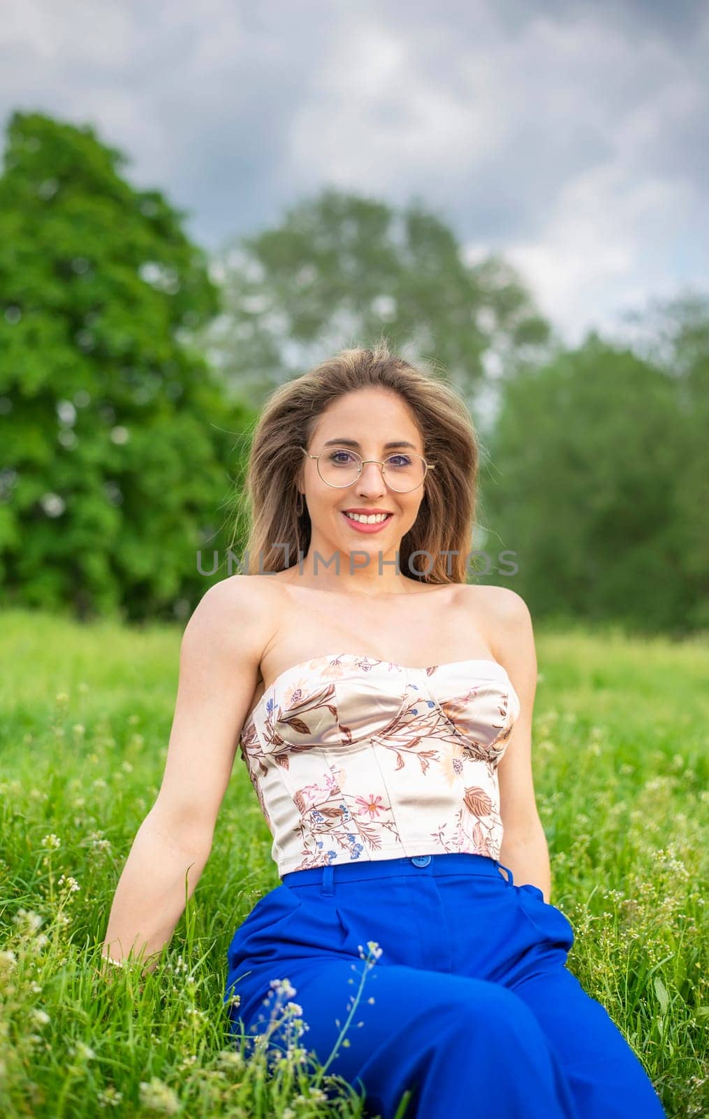 young woman with glasses sitting on a meadow