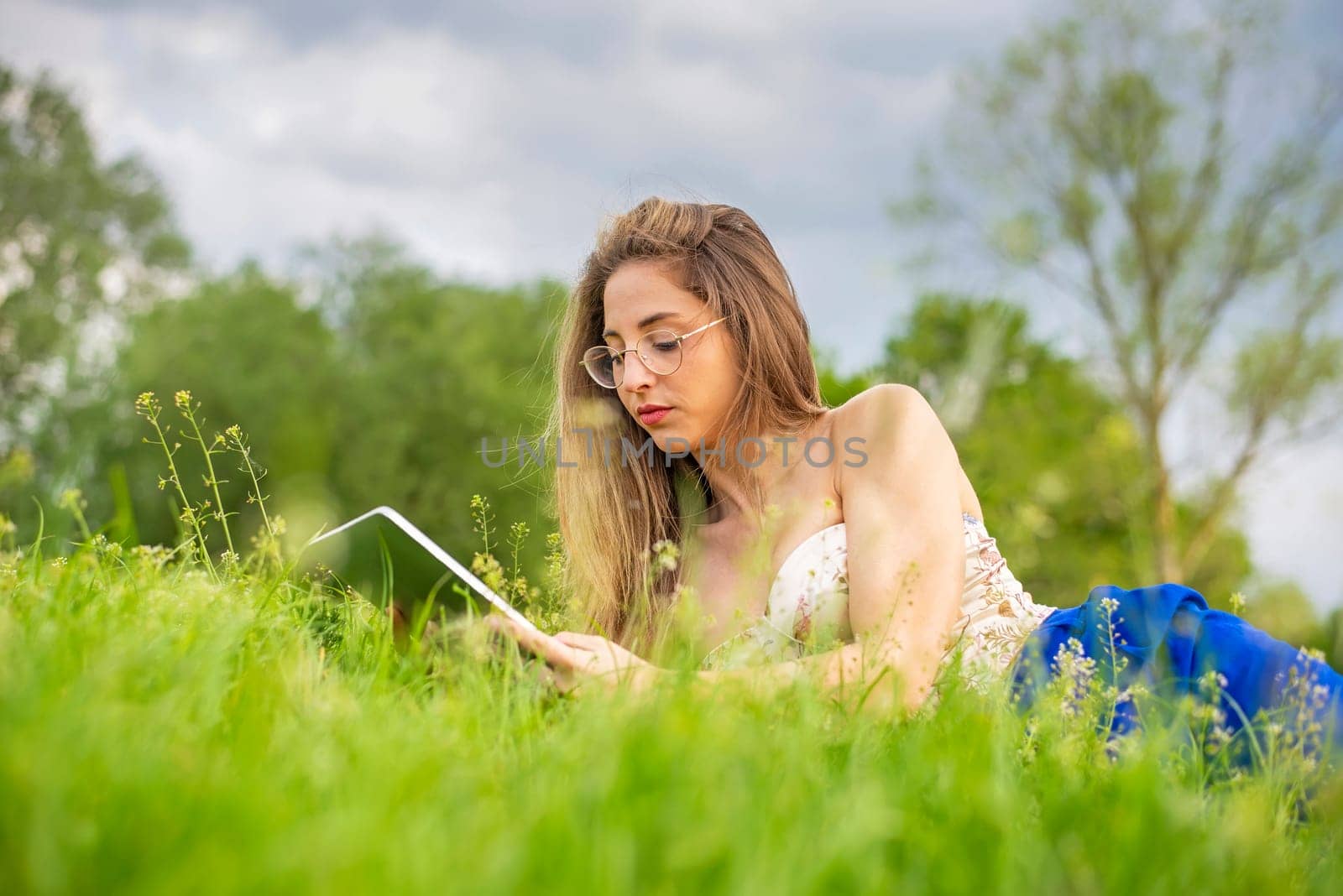 happy young woman with digital tablet lying on a meadow
