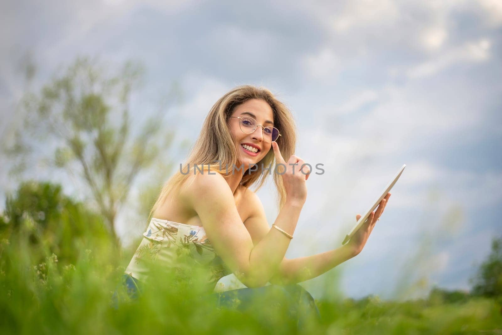 happy young woman with digital tablet sitting on a meadow