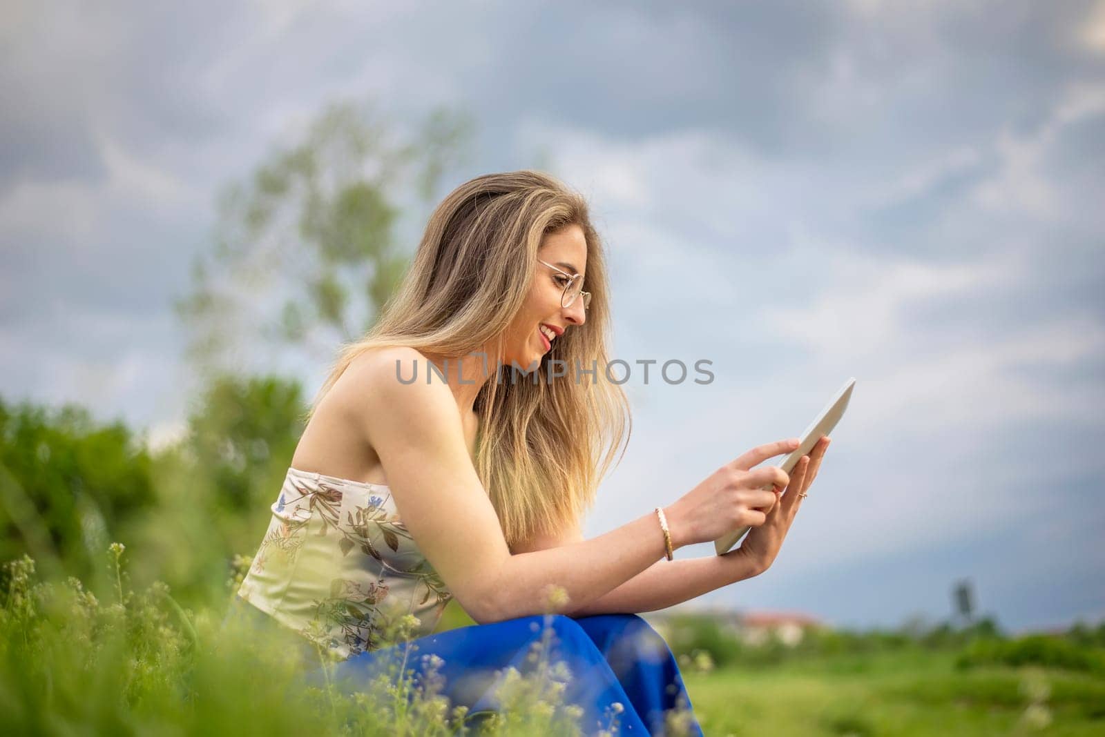 happy young woman with digital tablet sitting on a meadow