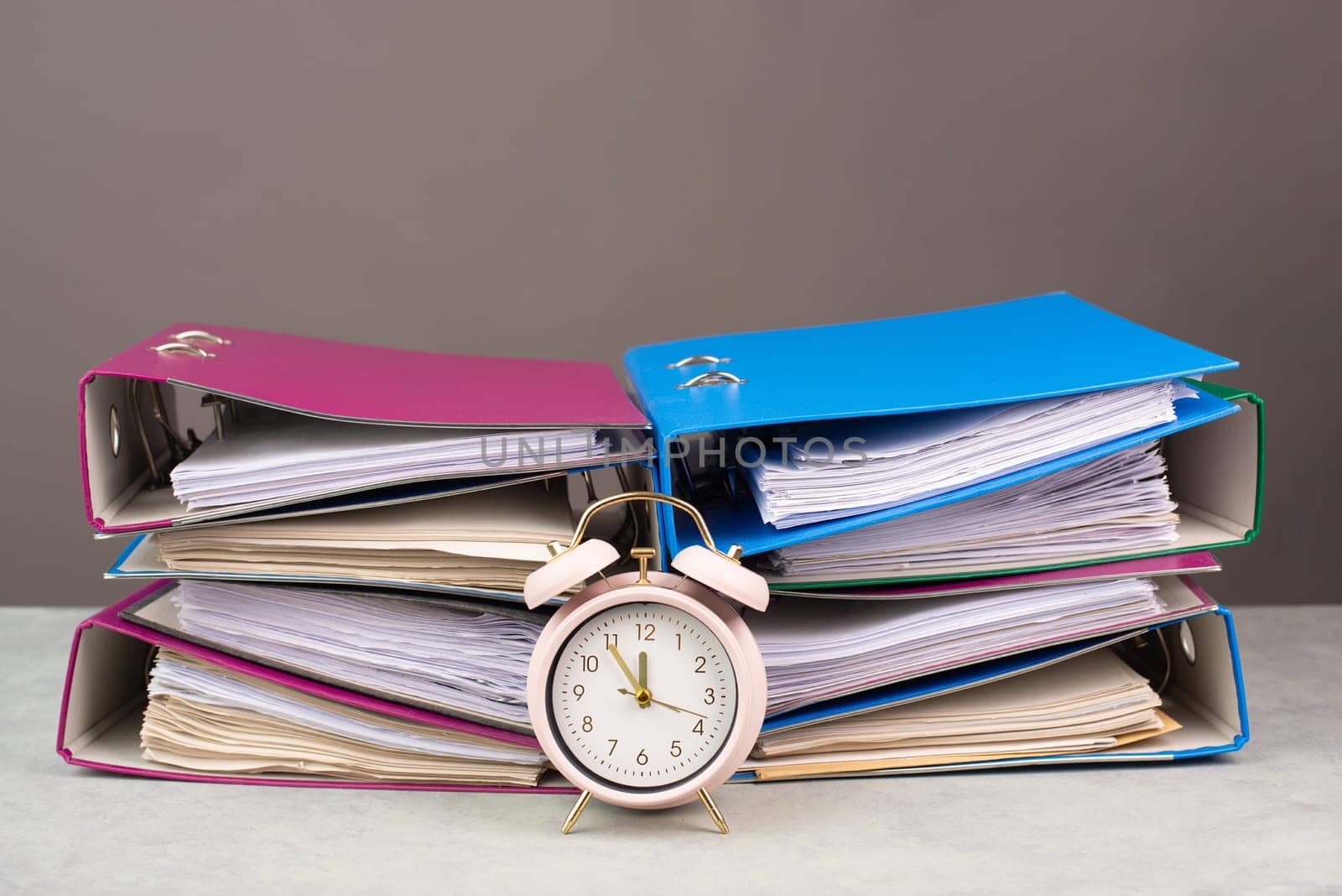 Alarm clock standing next to pile of file folders, burnout, stress and overworked, pressure at work, deadline