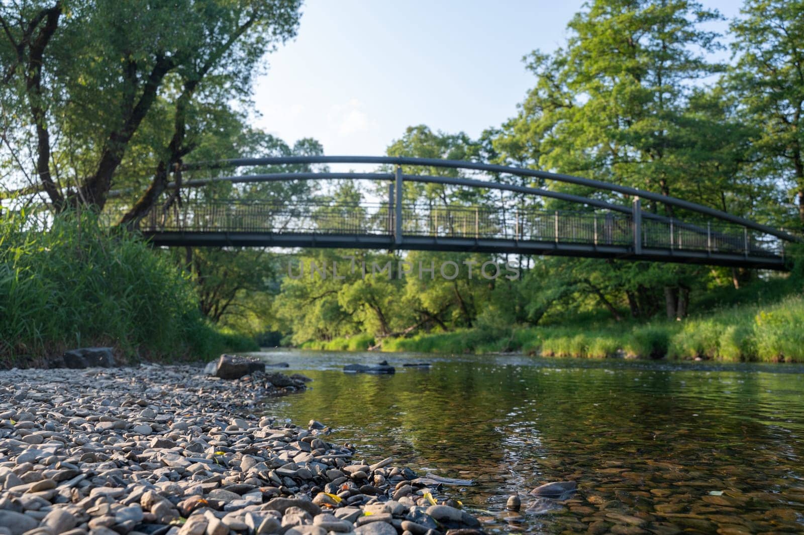 Pebbles on the river bank with a blurred background of green nature and a bridge