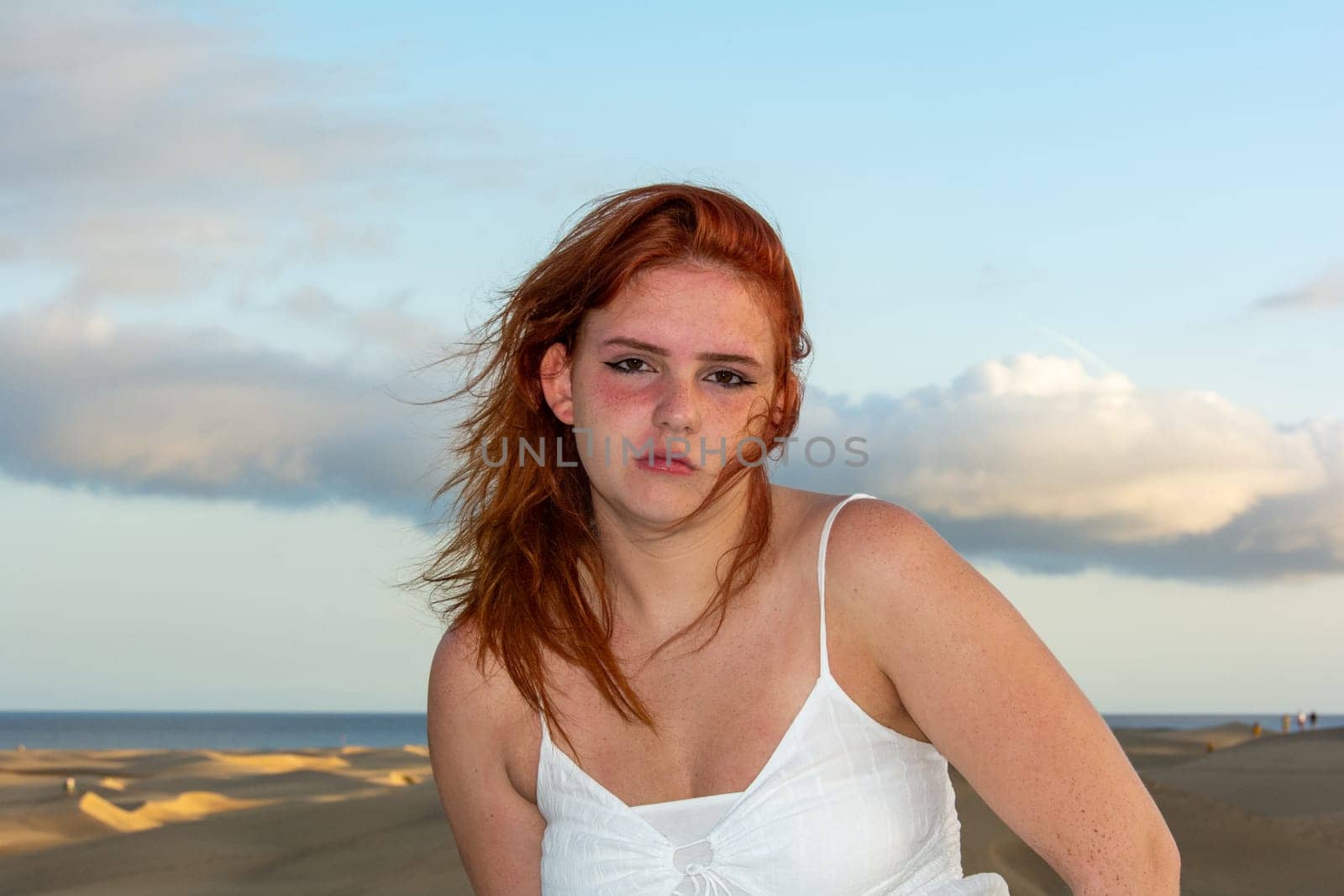 Young girl with red hair, on the beach in summer, her hair tousled by the wind