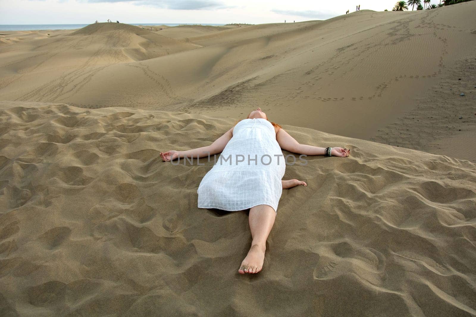 A young girl lies in the sand dunes in a white dress