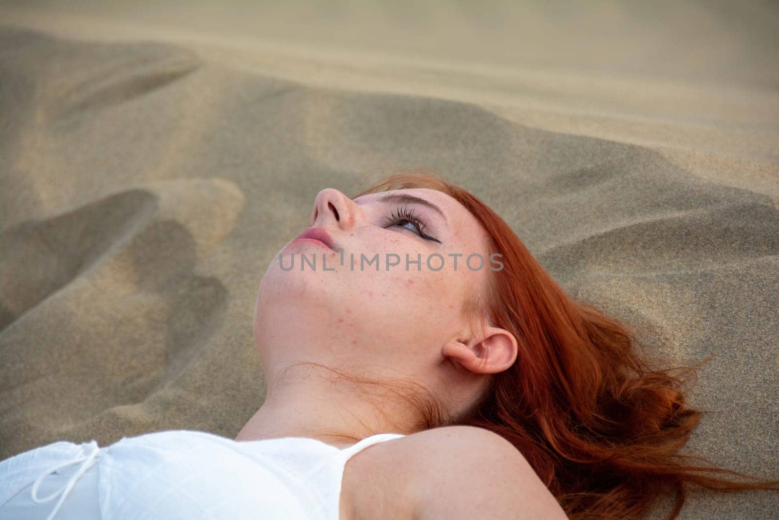 A young girl lies in the sand dunes in a white dress