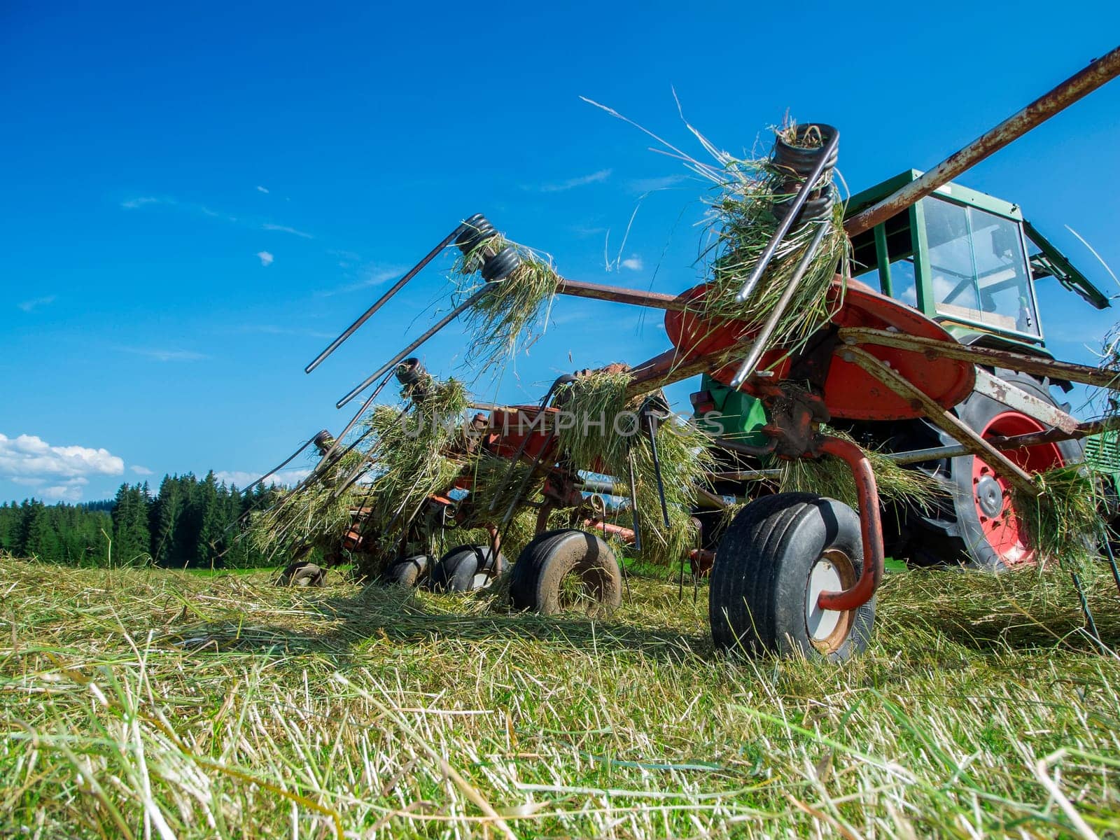 Low-level wide-angle view of a hay tedder on a small tractor in the Allgäu.