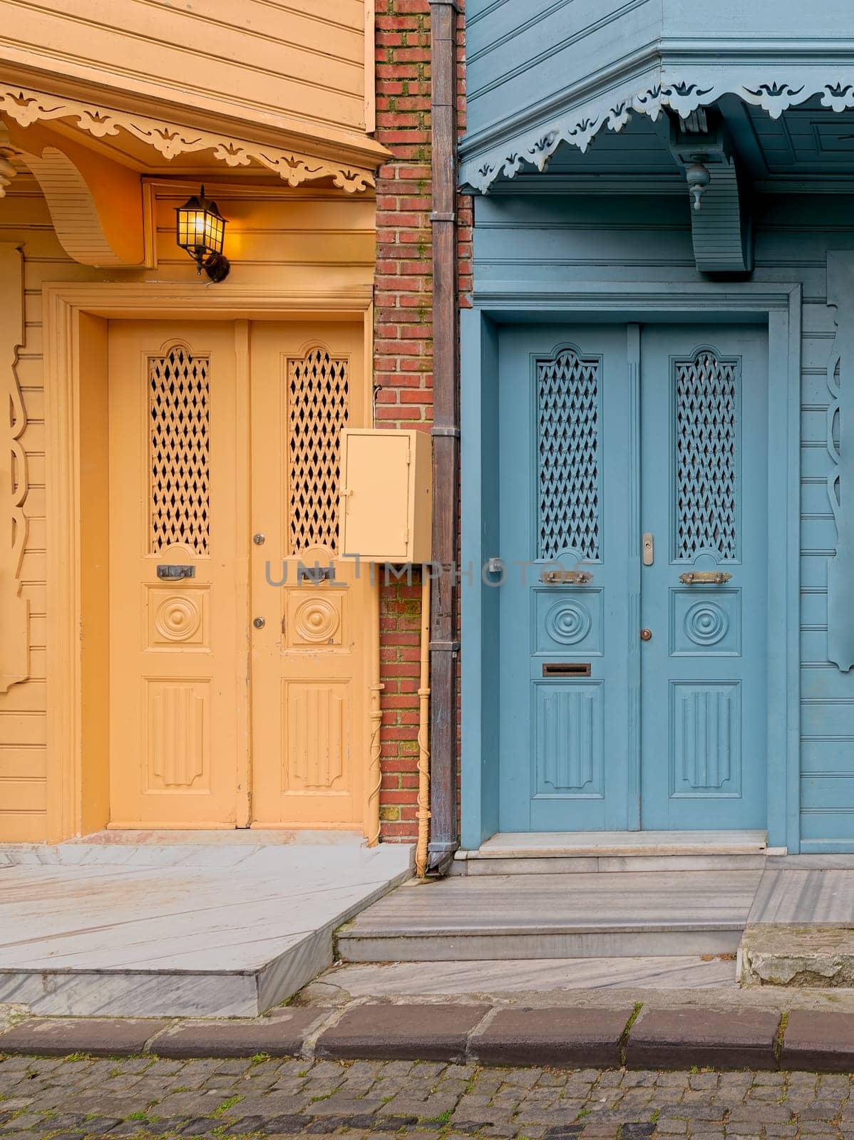 A pair of brightly colored doors, one in a deep turquoise blue and the other in a sunny lemon yellow, stand side-by-side on a narrow cobblestone street in Kuzguncuk neighborhood, Istanbul, Turkey