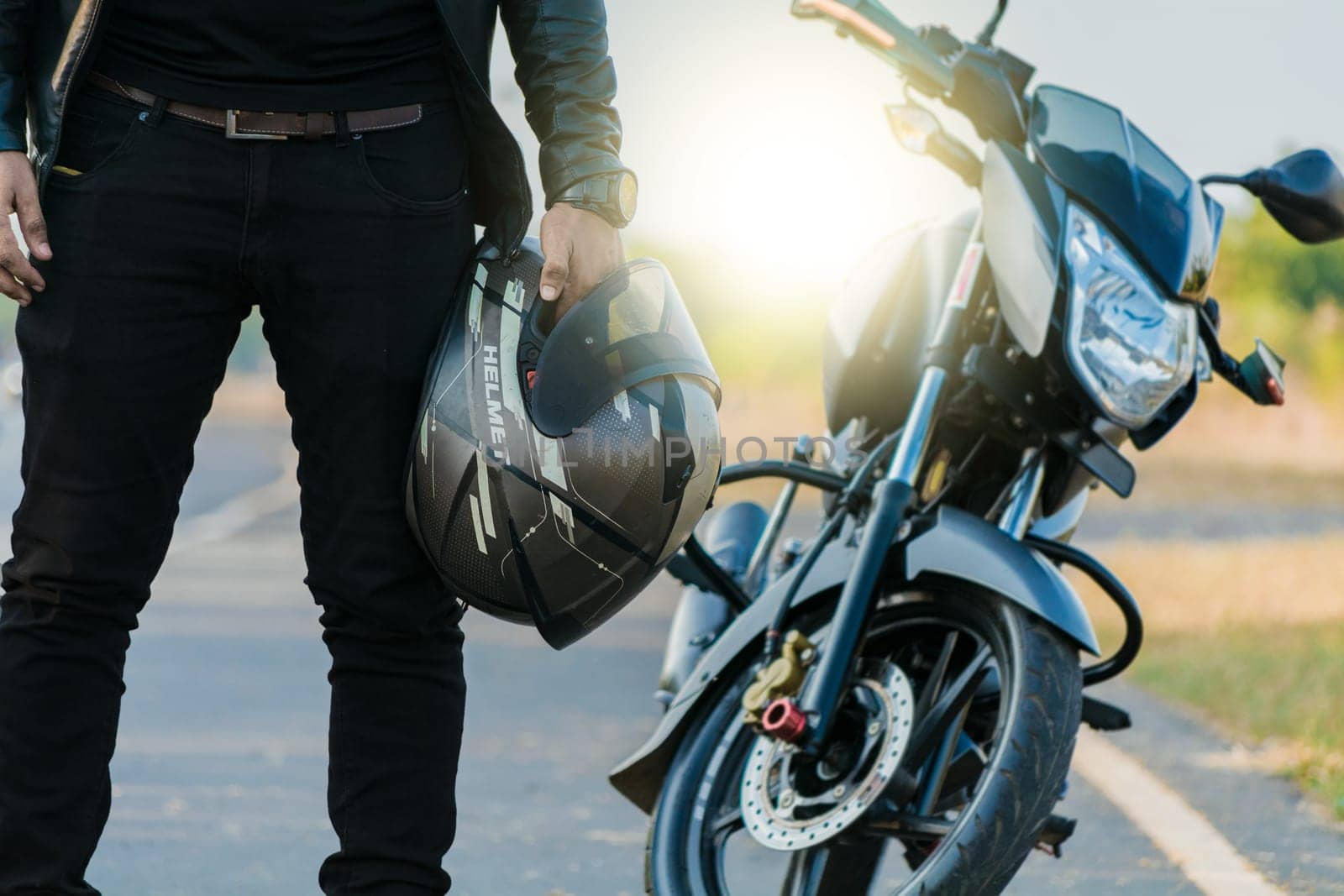 Unrecognizable biker holding helmet next to motorbike near the road. Motorcyclist holding safety helmet next to his motorbike near the road. Motorcycle safety helmet concept
