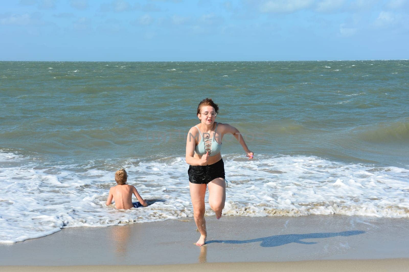 Two children have fun in the waves on the sea beach, Girl runs out of the water, boy sits in the waves