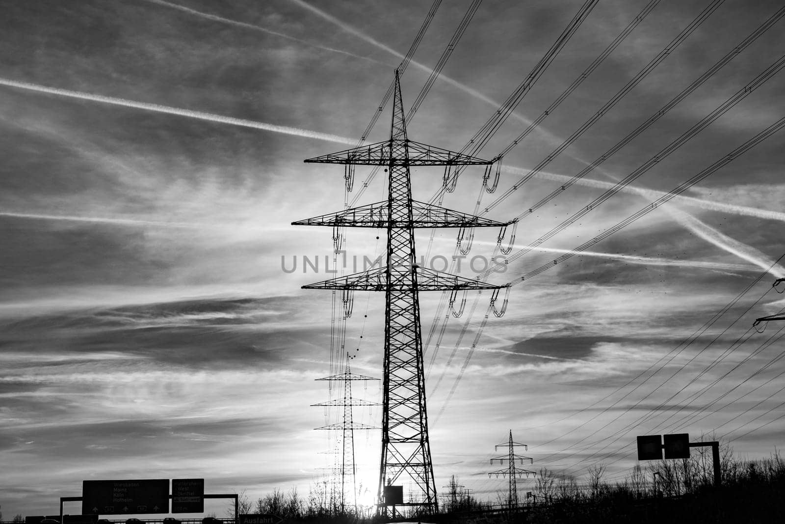 scenic sunset seen from highway with electric pylon and condensation stripes from aircrafts at the sky