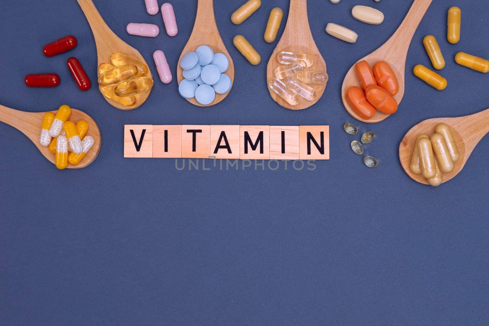 Different vitamins in wooden spoons with text on gray background. Pills, drugs, supplements, medicine, pharmacy and healthcare concept.