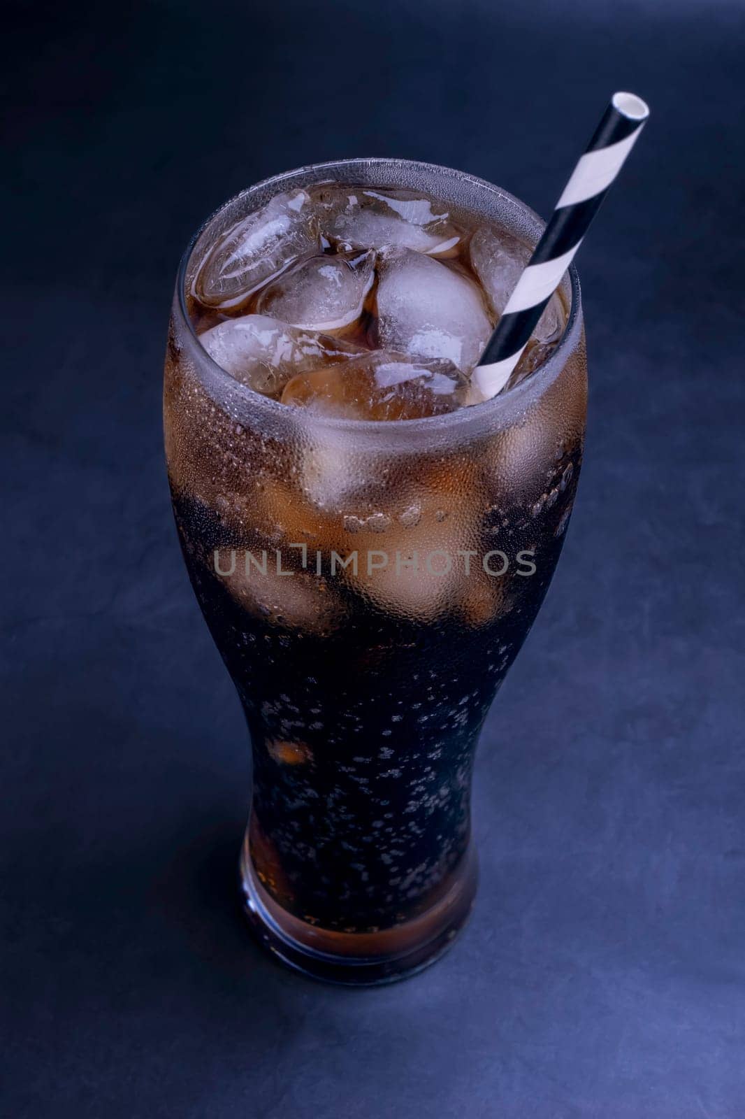 Cool glass of cola drink with ice, bubbles and fizz. Fresh cold sweet with ice cubes. Cola glass with summer refreshment on black.