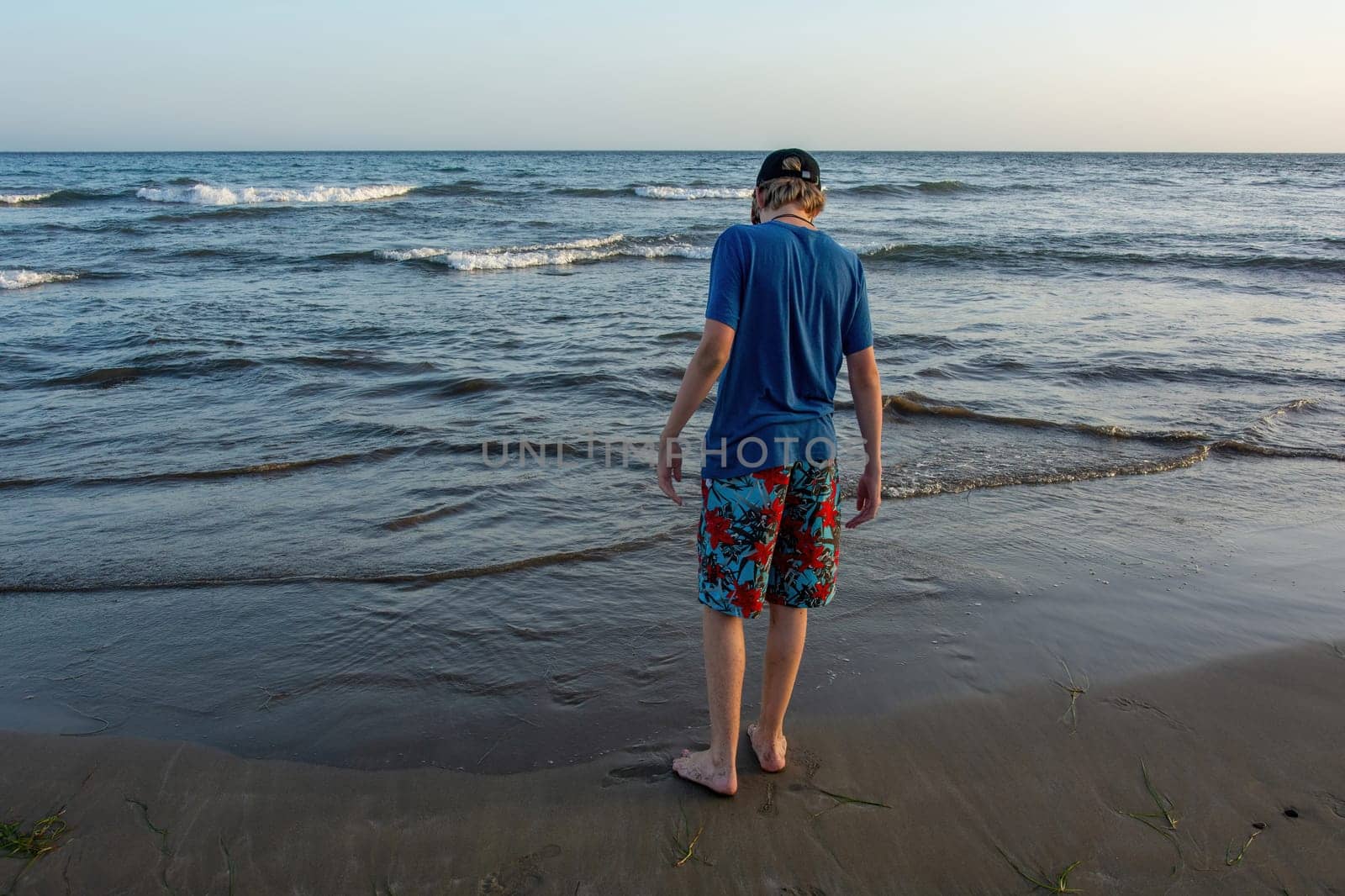 A boy wearing shorts and a cap stands on a sandy beach by the sea, with a blue sky,A boy wearing shorts and a cap stands on a sandy beach by the sea, with a blue sky