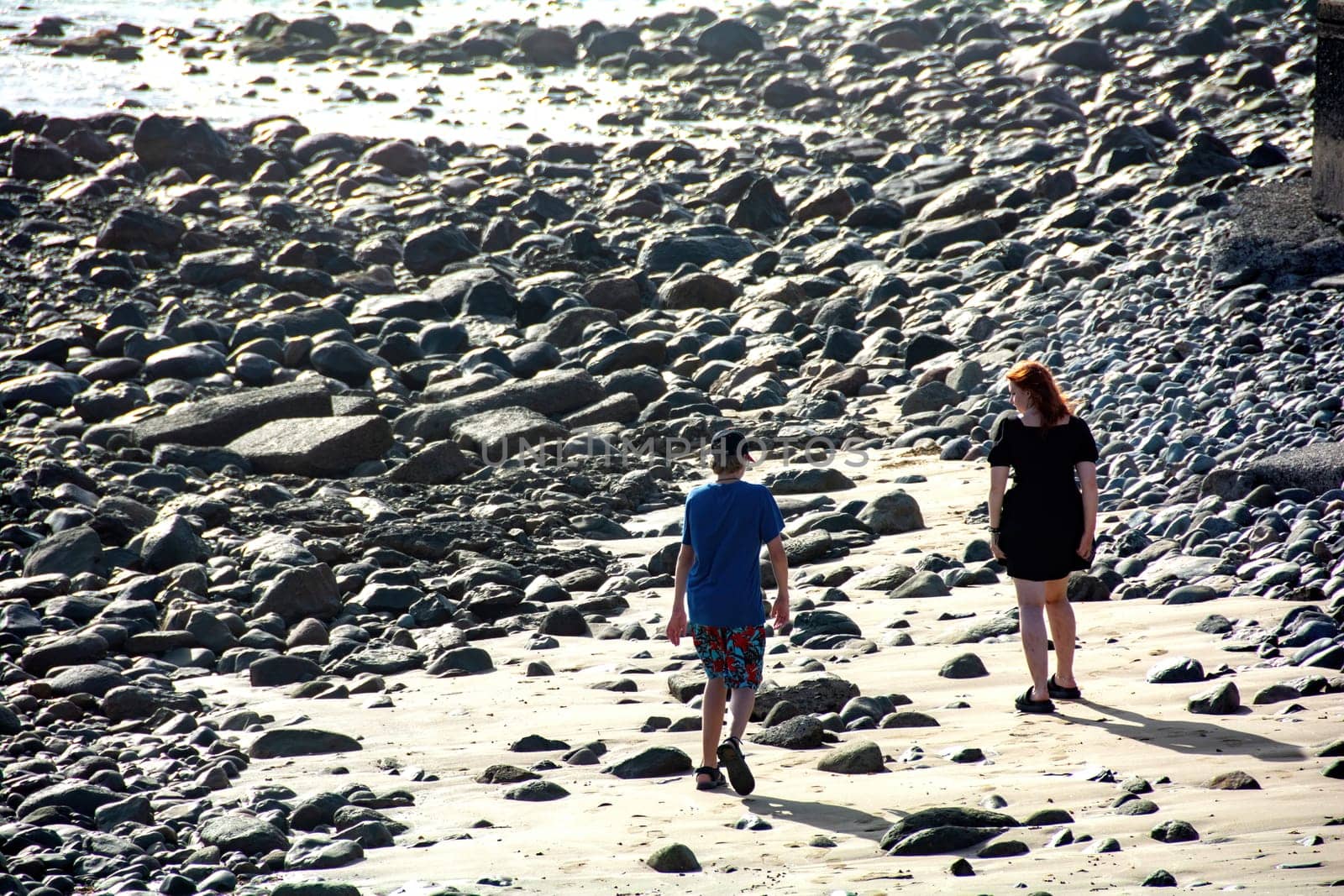 Young woman with a short black dress and a boy on a stony beach,Young woman with a short black dress and a boy on a stony beach