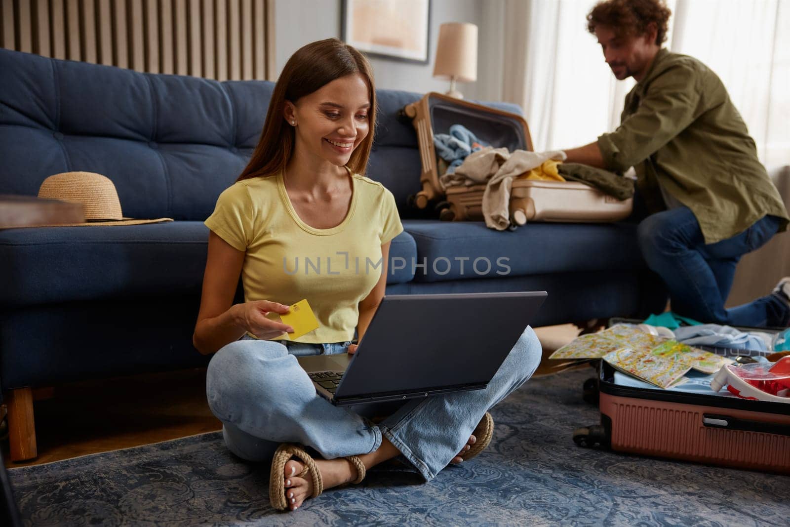 Wife booking ticket paying for hotel using laptop and bank credit card while husband preparing luggage bag for trip adventure. Planning vacation travel concept