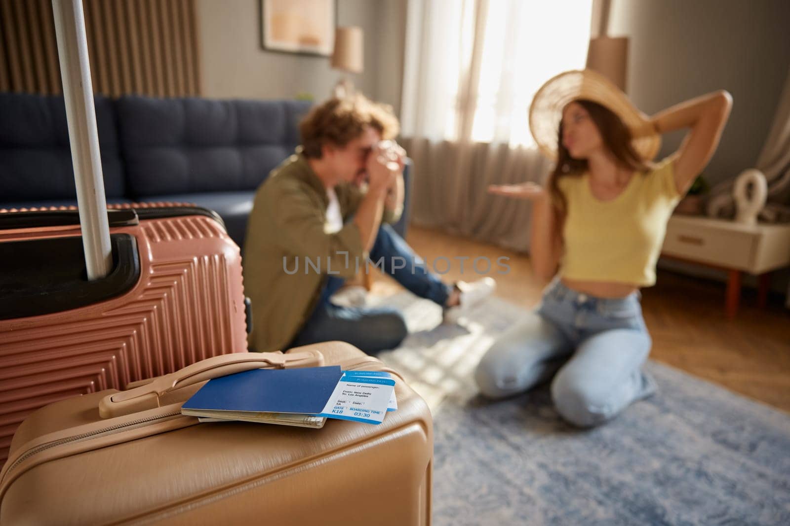 Preparation for trip, planning vacation and going for resort leisure activity. Loving man shooting with digital camera adorable woman in straw hat at home. Packed baggage and documents on foreground