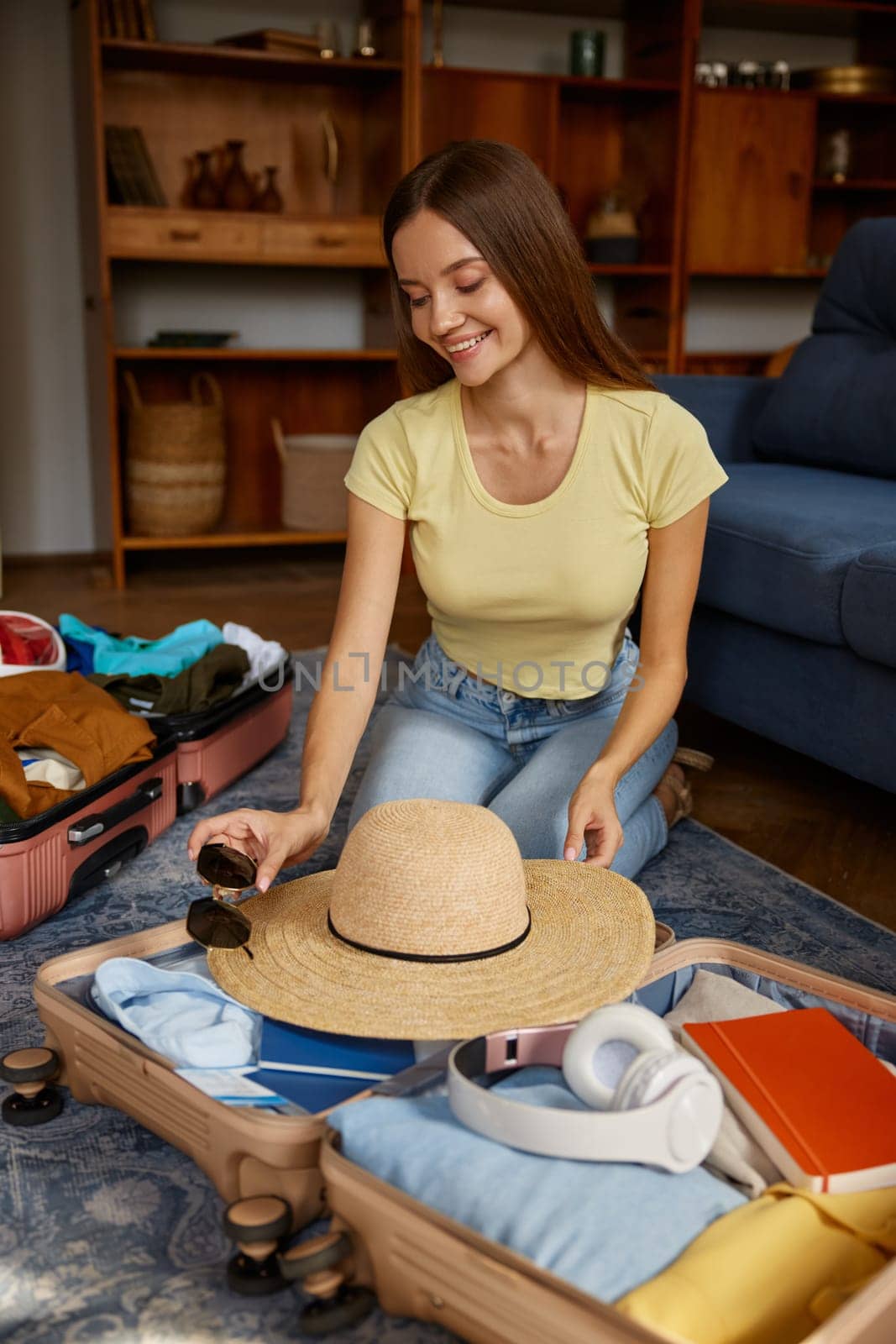 Young smiling woman putting sunglasses into travel bag with summer clothing while packing stuff for travel. Summer vacation trip adventure aspirations concept