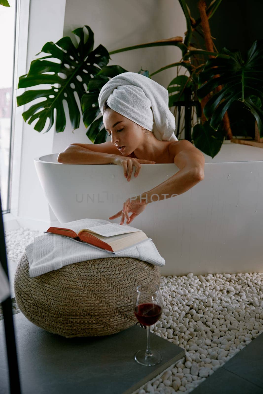 Relaxed woman bathing and enjoying reading book with wine. Pleasant rest time at home concept