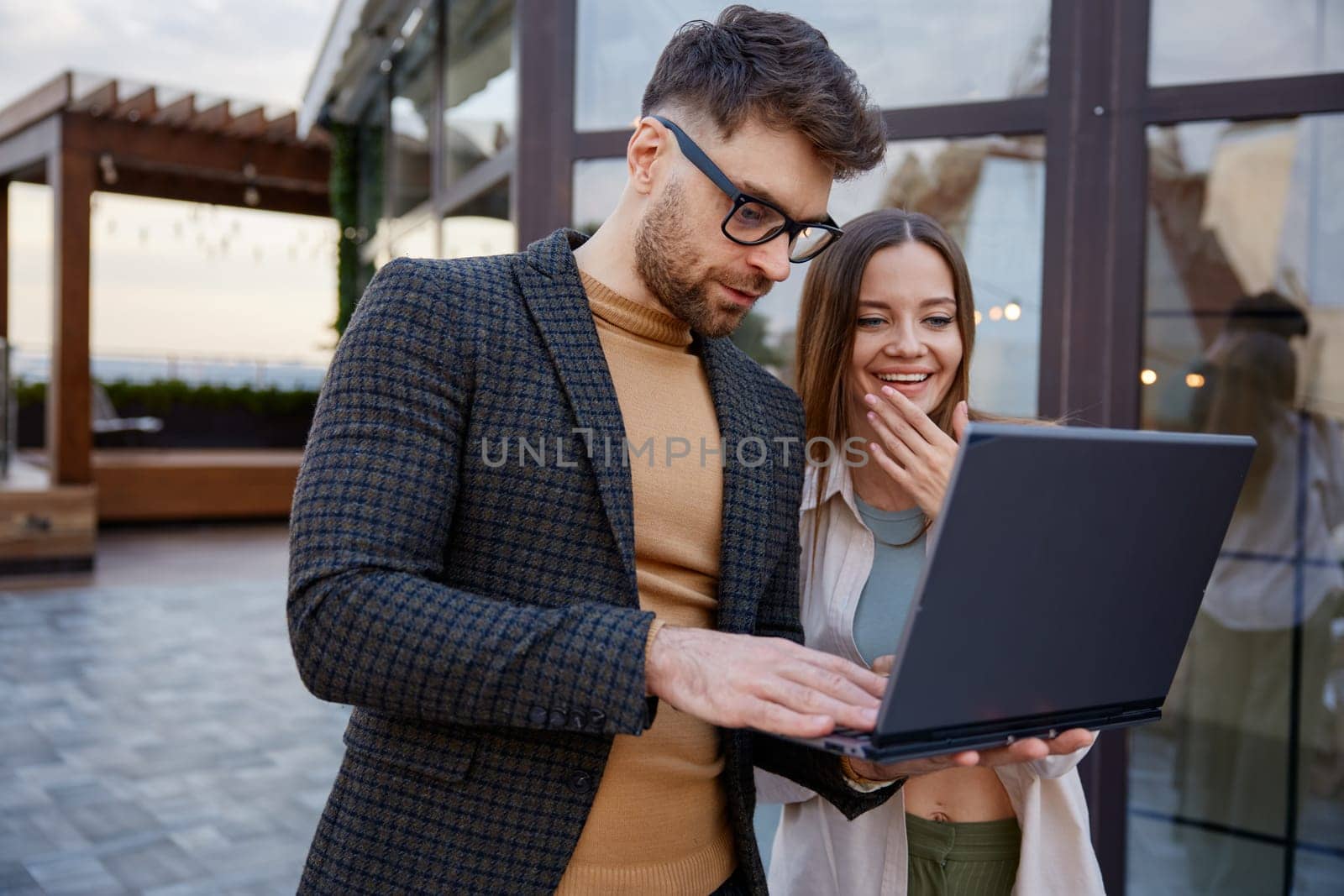 Man and woman using laptop standing together on roof terrace. Young freelancers discussing online business project