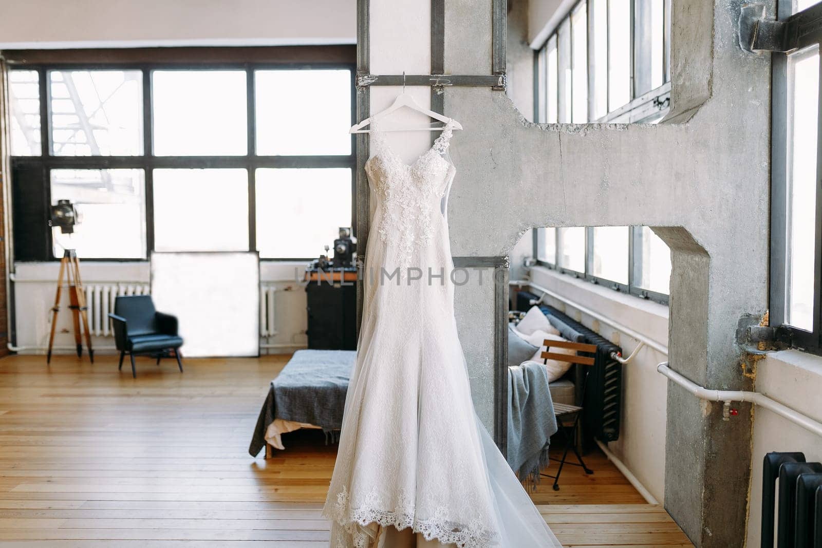 A white long wedding dress is hanging on a hanger in a larger studio