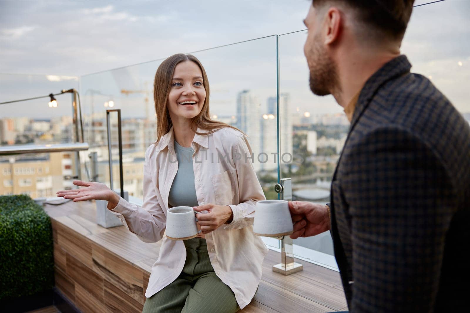 Man and woman coworkers having nice conversation sharing ideas emotionally speaking at balcony. Freelancers team taking coffee break during workday in office
