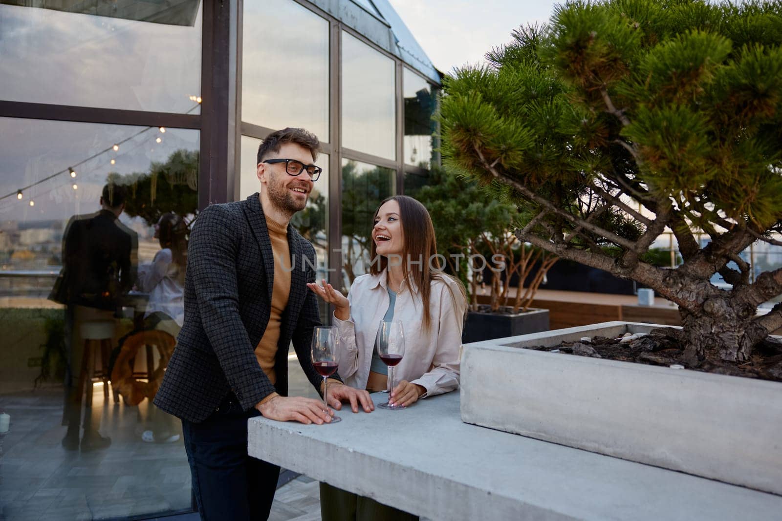 Young man and woman business colleagues talking drinking wine during corporate rooftop party. Teambuilding and social gathering