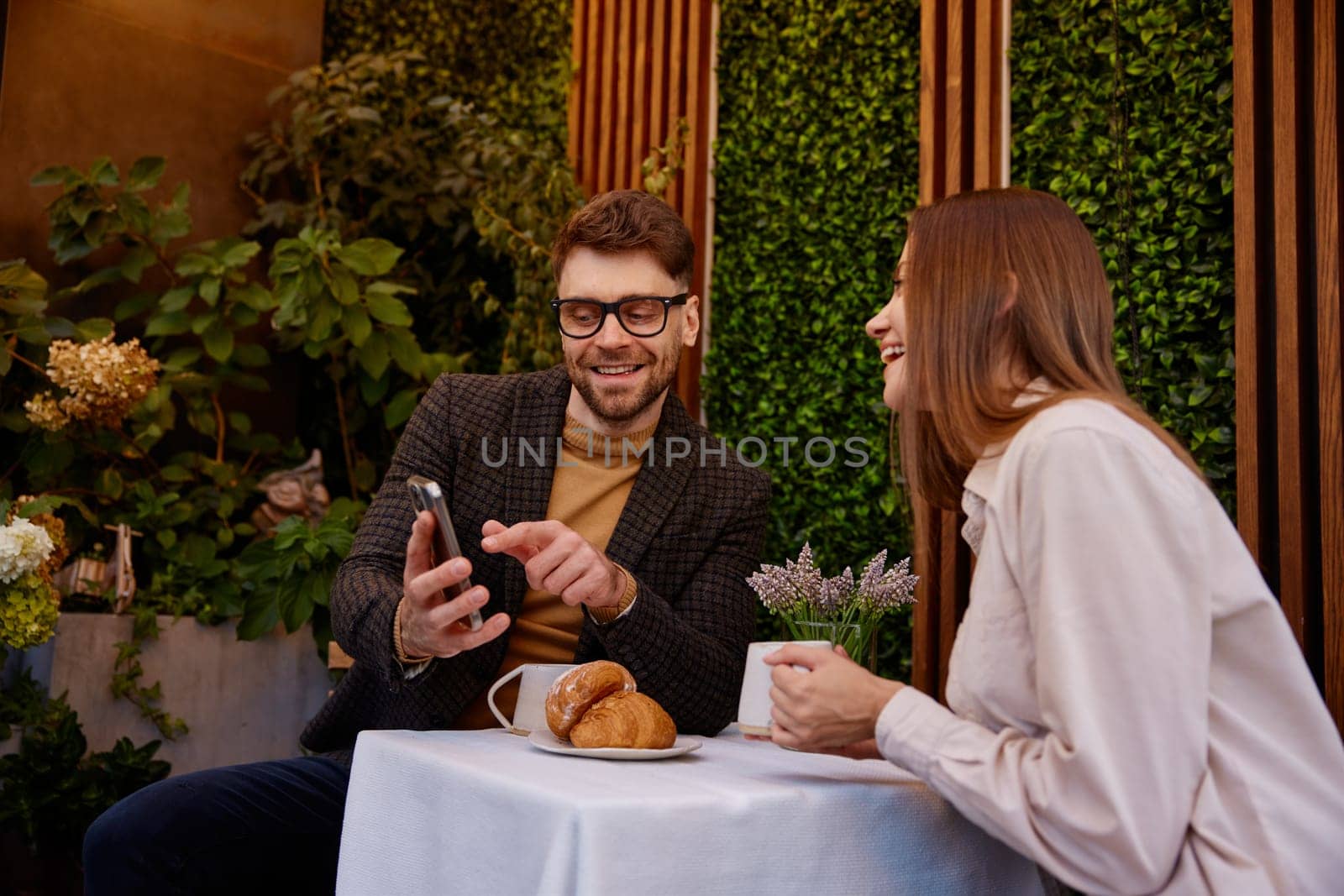 Young man and woman talking using mobile phone having business meeting in cafe. Carefree businesspeople viewing social media networks enjoying relaxing moment during work break