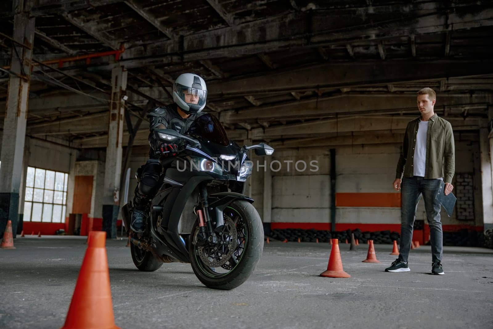 Man motorcyclist learning to ride bike at private school maneuvering between cones at indoor motordrome