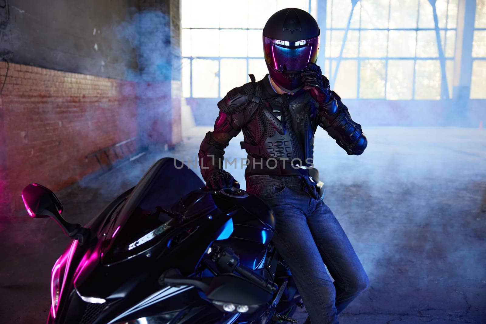 Portrait of man extreme rider sitting at motorcycle taking rest after training at driving school motordrome. Atmospheric photo in neon light illumination and smoke
