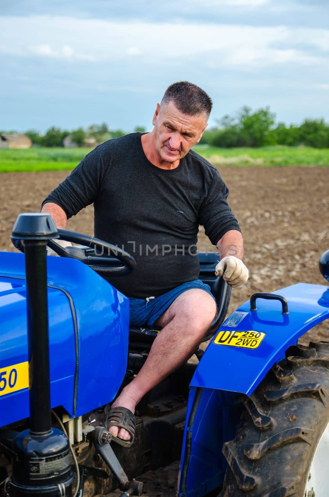 Kherson oblast, Ukraine - May 29, 2021: An elderly farmer sits and drives a tractor. Running a small agribusiness. Farming. Loosening, land cultivation. Mechanization in agriculture. Farm work.