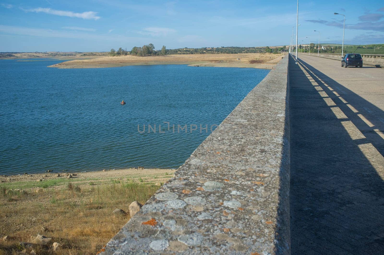 Float tube fisher close to Barragem do Caia wall, Campo Maior, Alentejo, Portugal. Car crossing the road