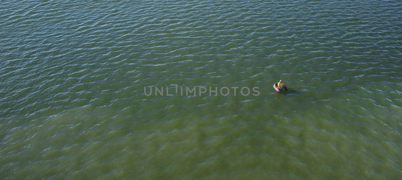 Float tube fisher floating over green waters of a reservoir. Long format
