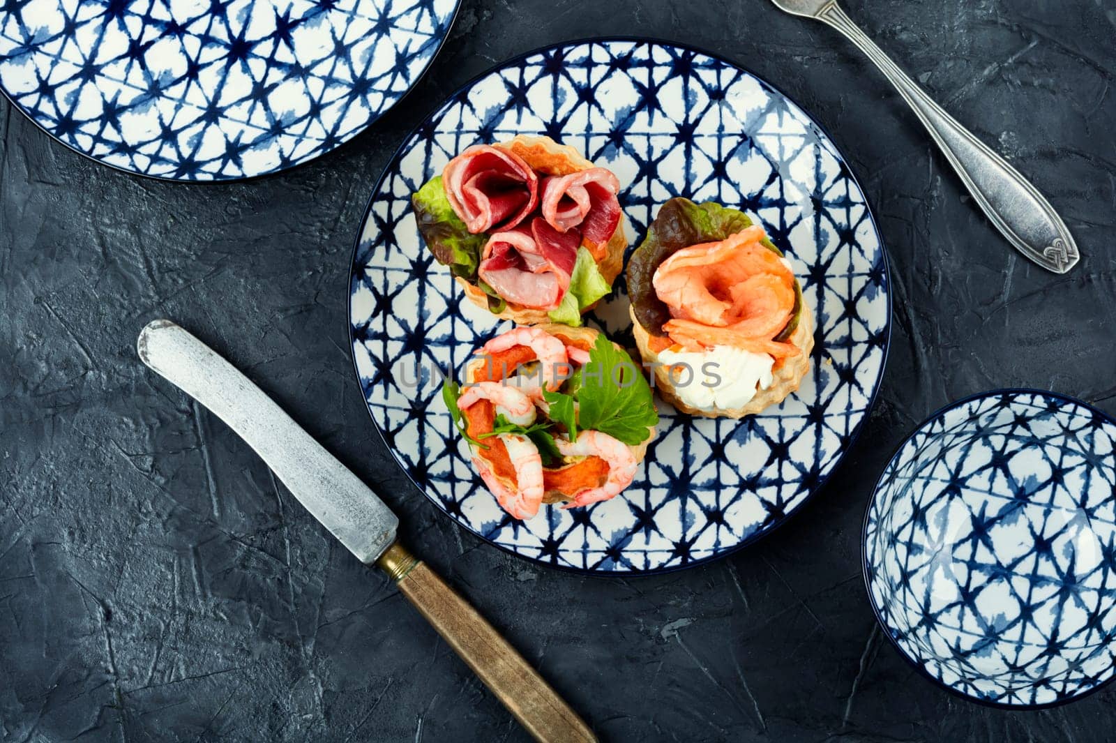 Puff pastry tartlets or canapes with fish, shrimp and bacon on a plate on the table.