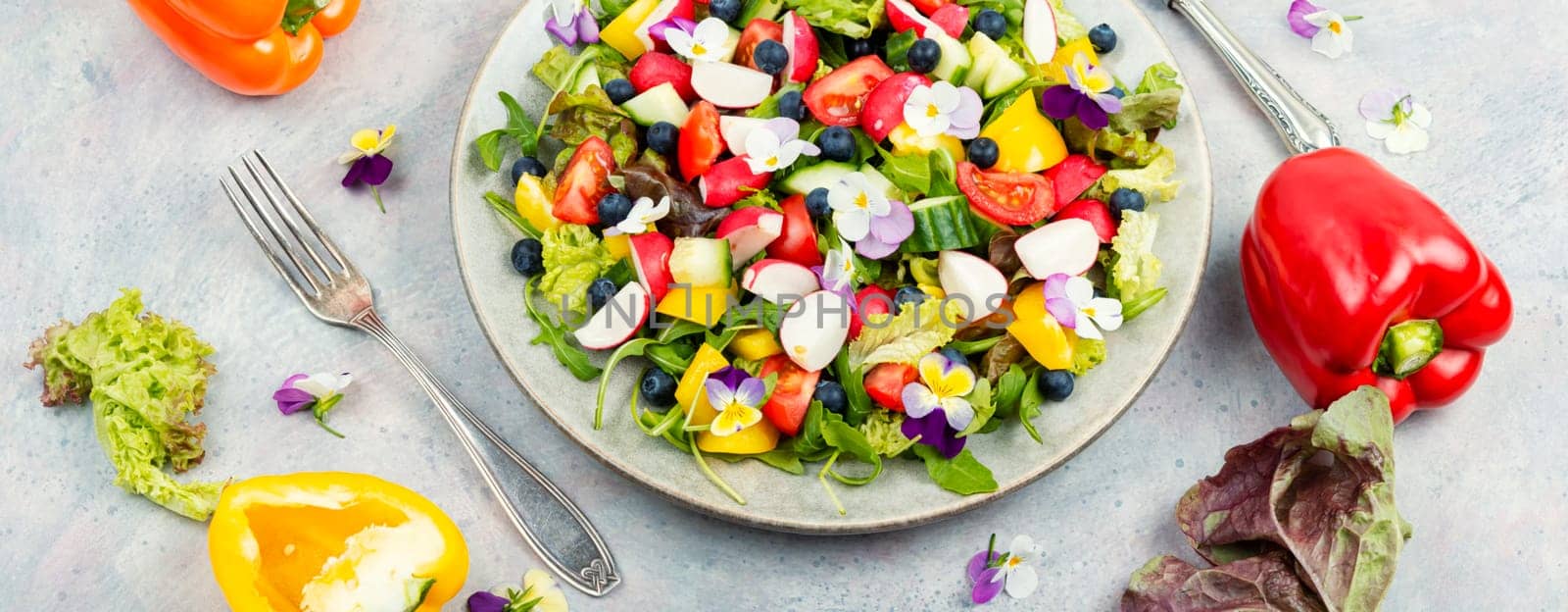 Spring salad of fresh vegetables decorated with edible flowers. Healthy salad.